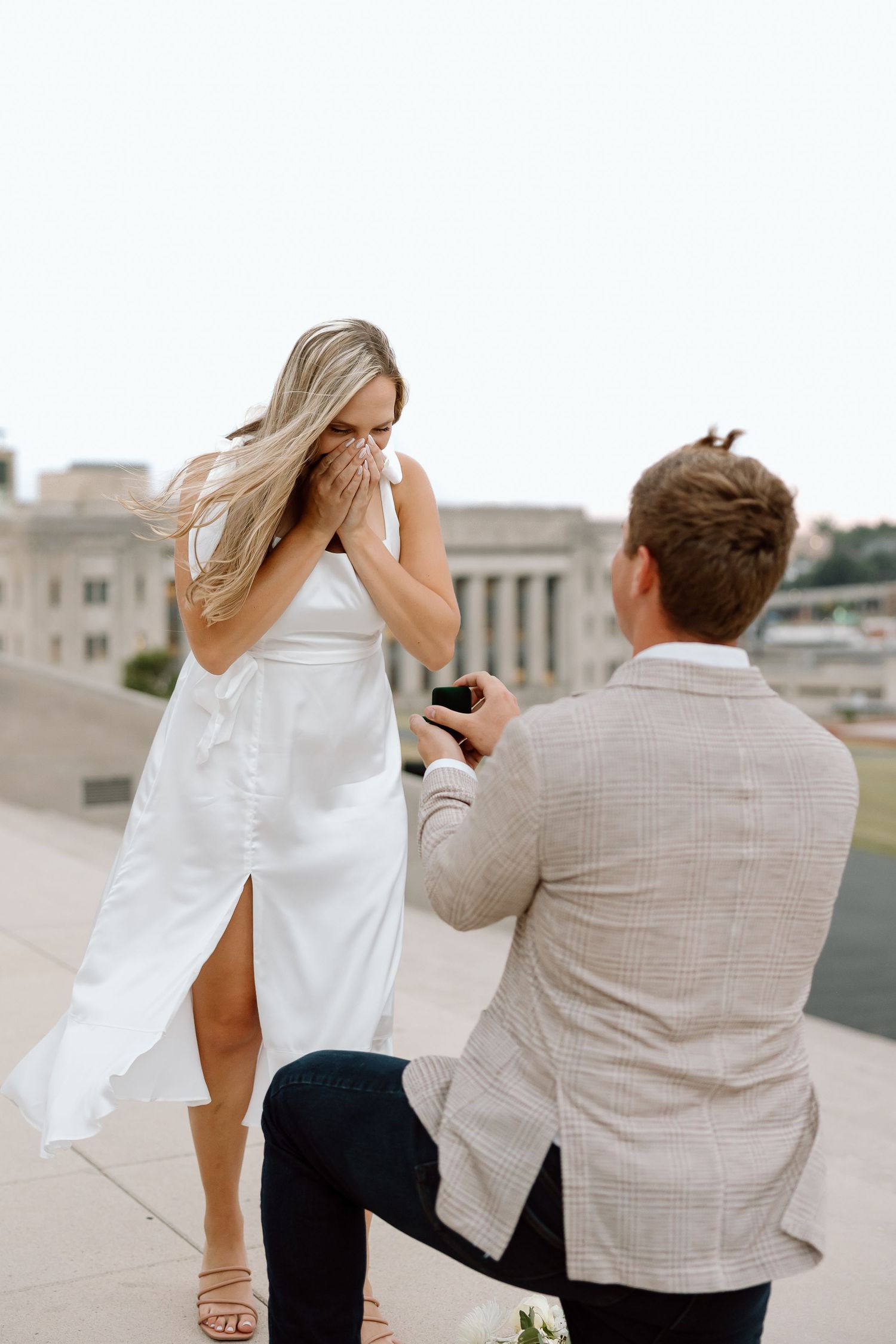 A romantic marriage proposal moment captured on an outdoor terrace with a city backdrop.