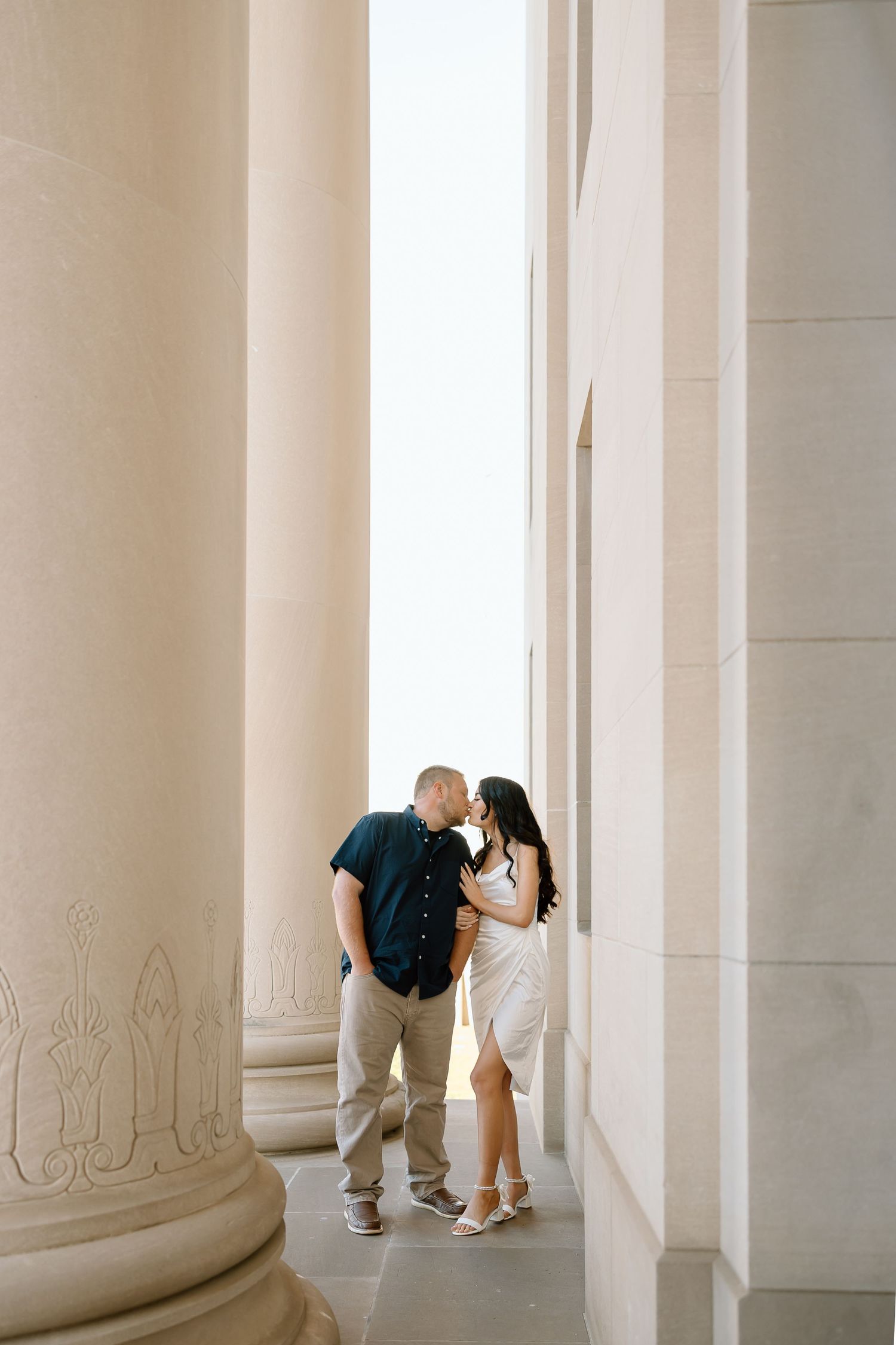 Couple shares romantic moment between elegant white columns in a classic architectural setting.