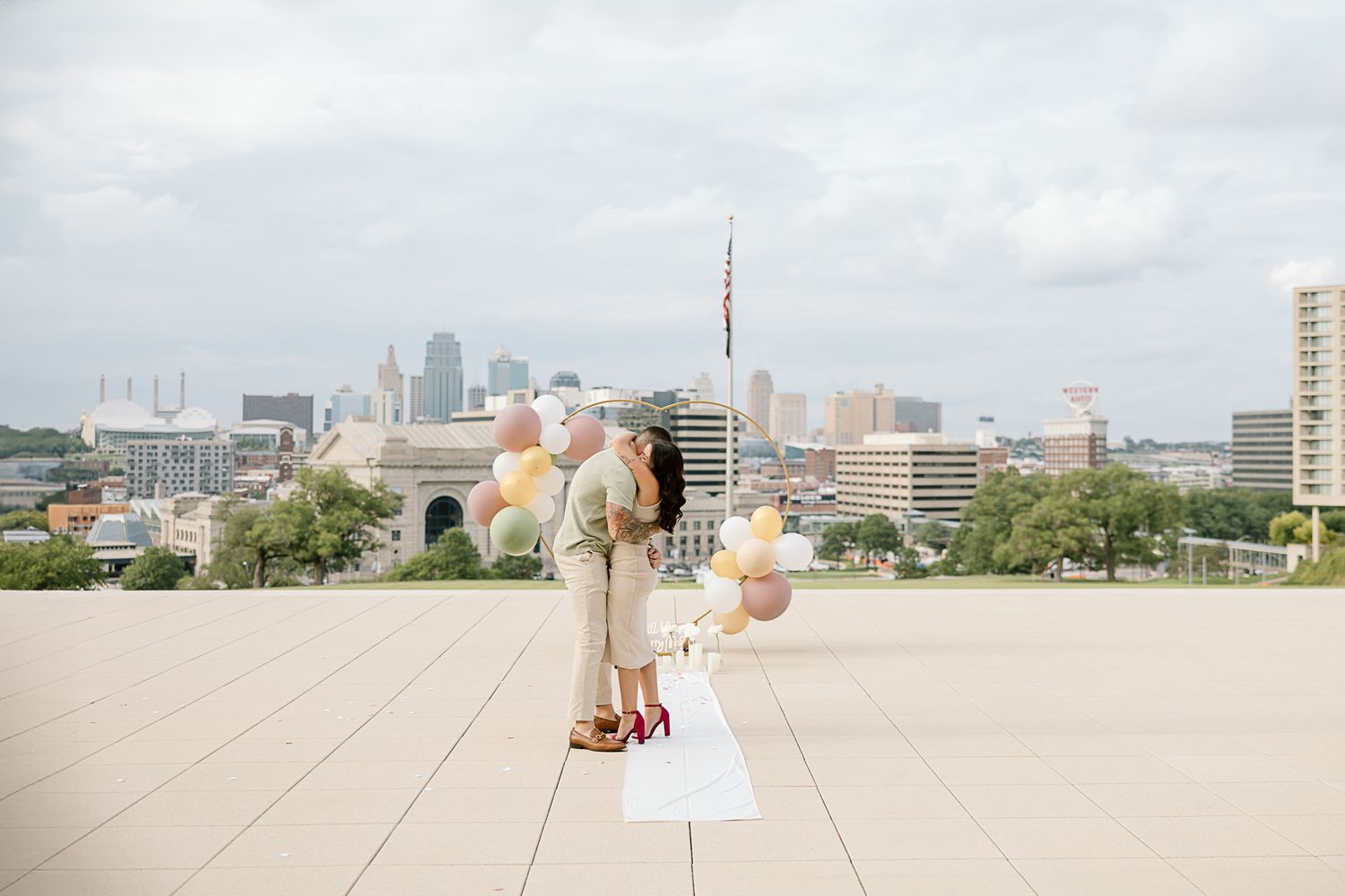 Couple standing on rooftop with colorful balloons against Kansas City downtown skyline.