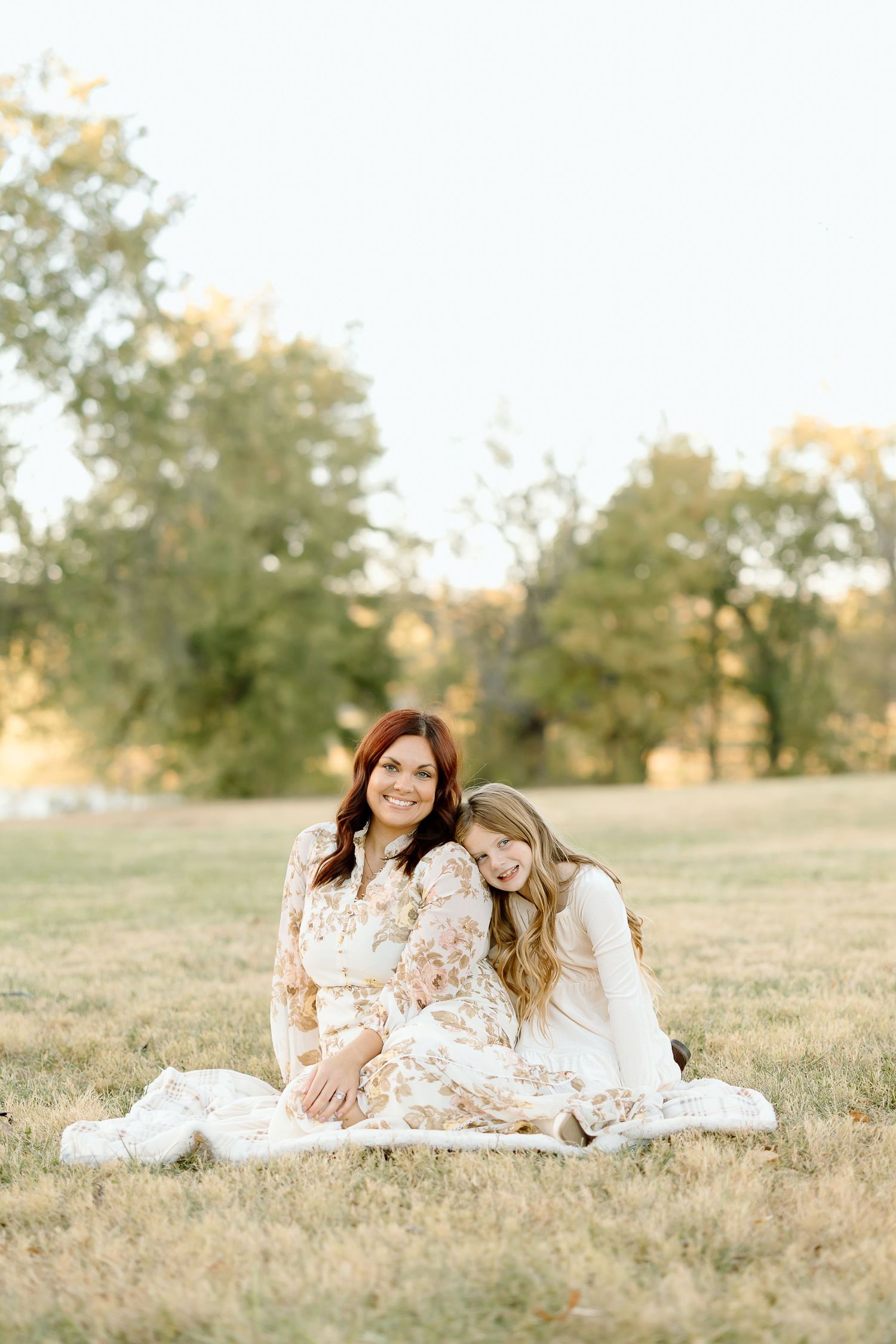 Two people in floral dresses laying on grass in a sunny field during a golden hour photoshoot.