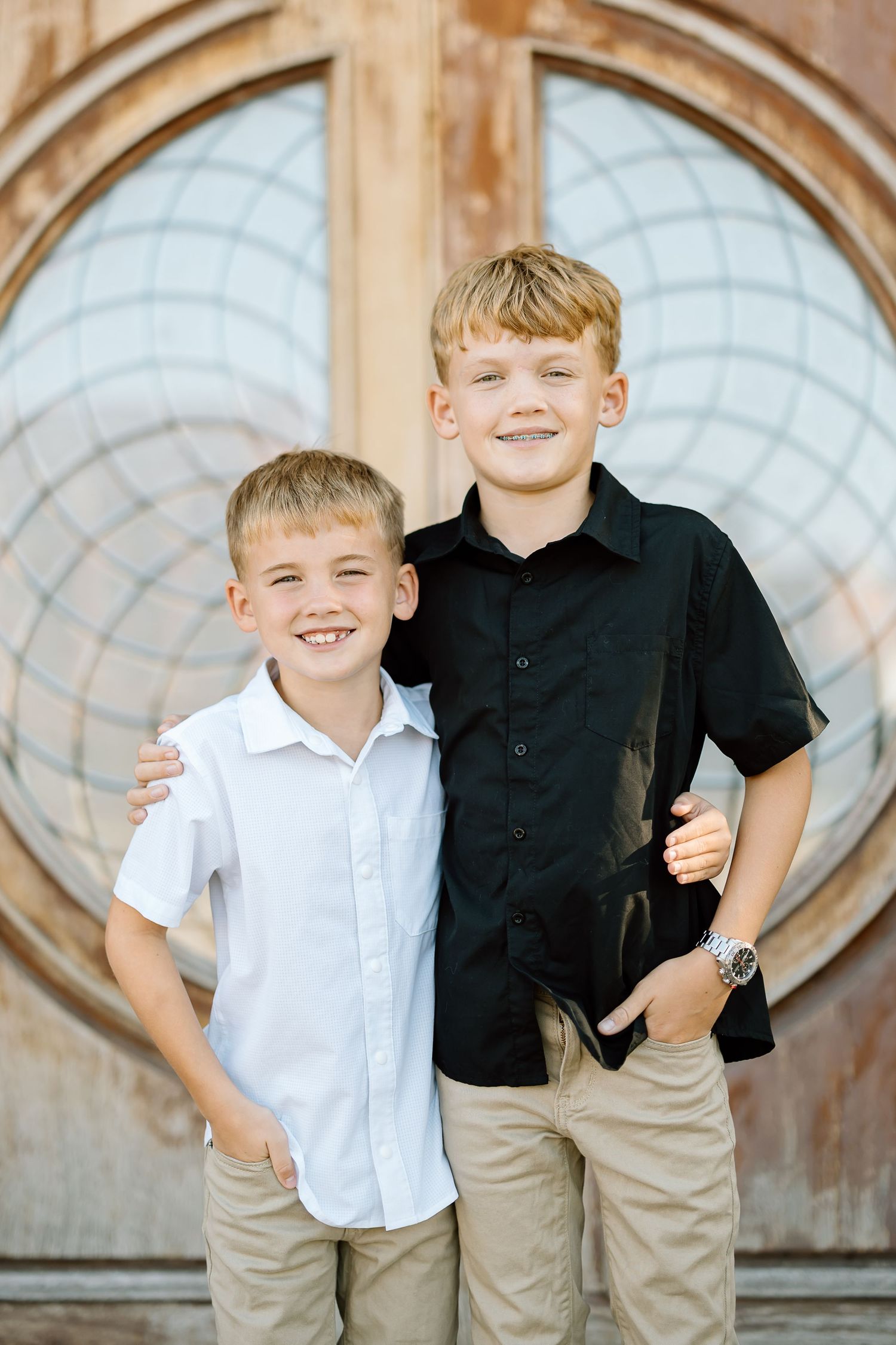 Two young children in white and black shirts pose together in front of an ornate architectural background.