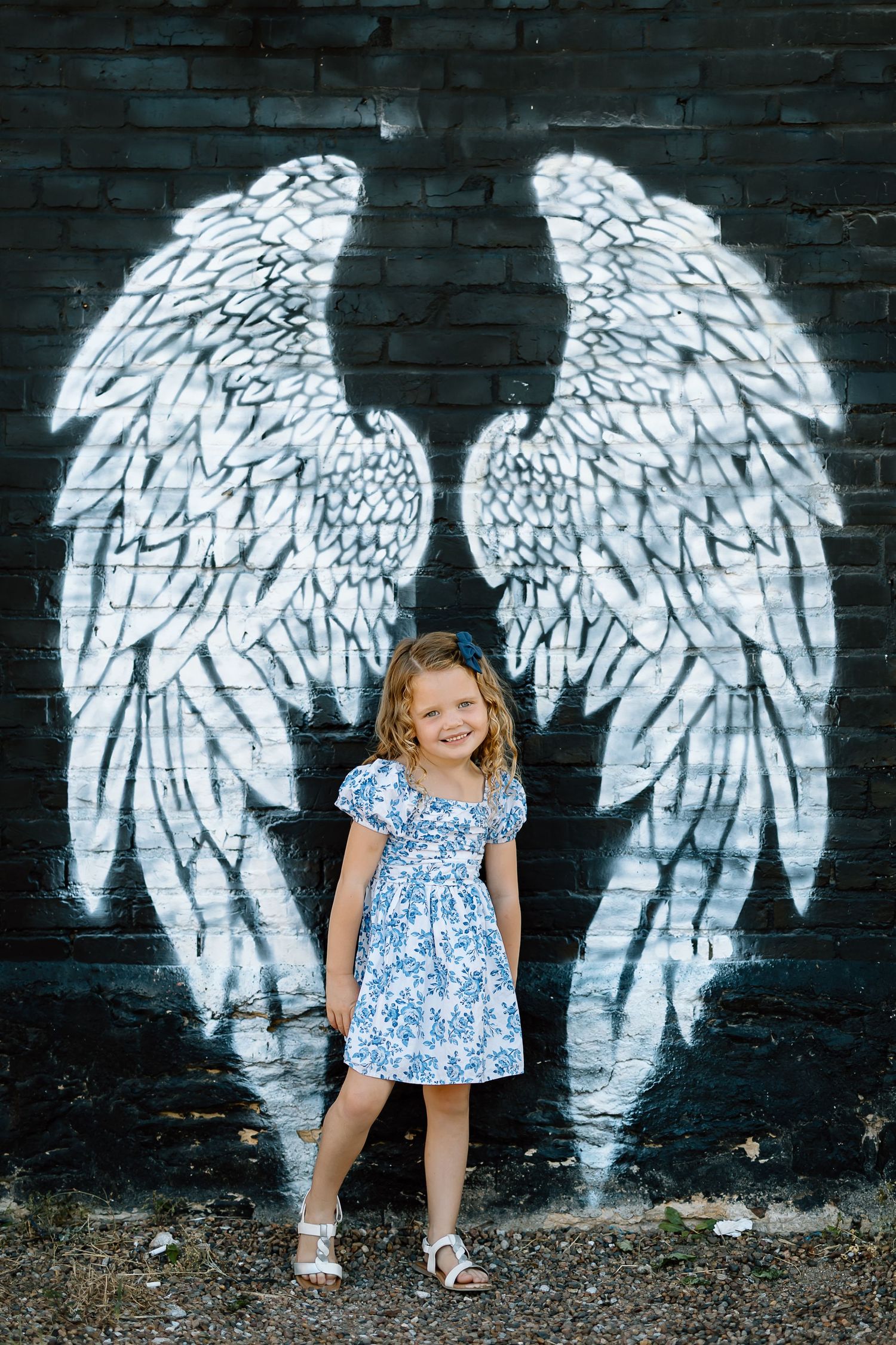 A series of photos showing white angel wings painted on a dark brick wall creating an interactive street art backdrop.