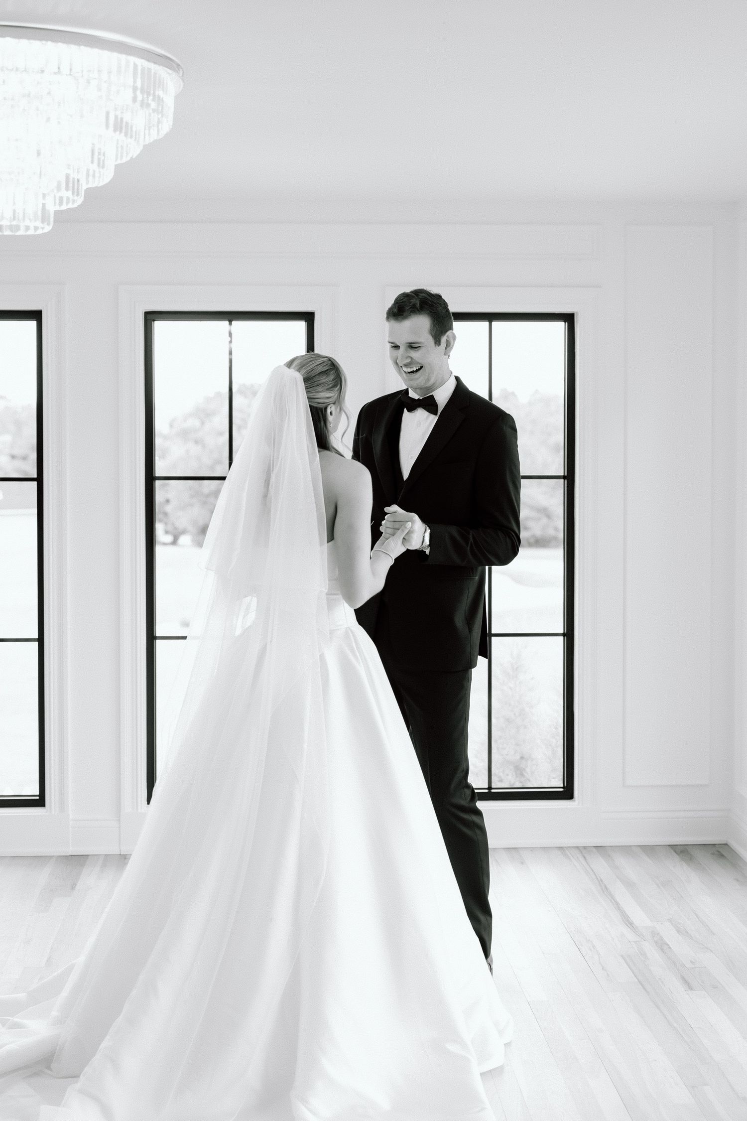 Black and white photo of a bride and groom sharing their first dance in an elegant white room with chandelier.