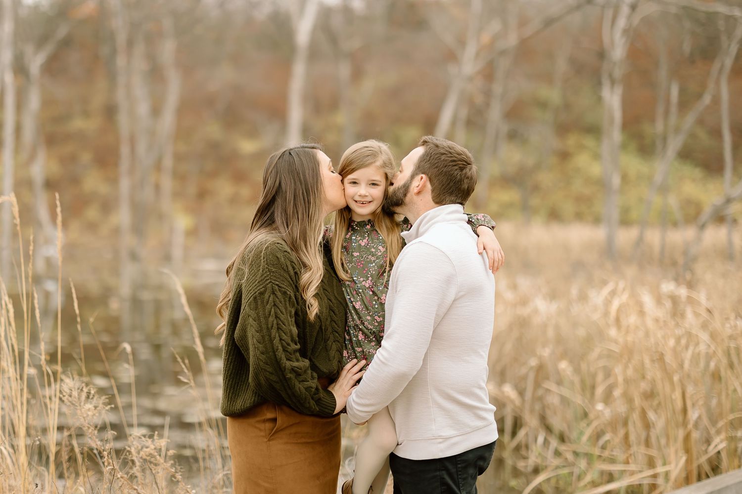 Sweet family moment captured during outdoor autumn photoshoot near water.
