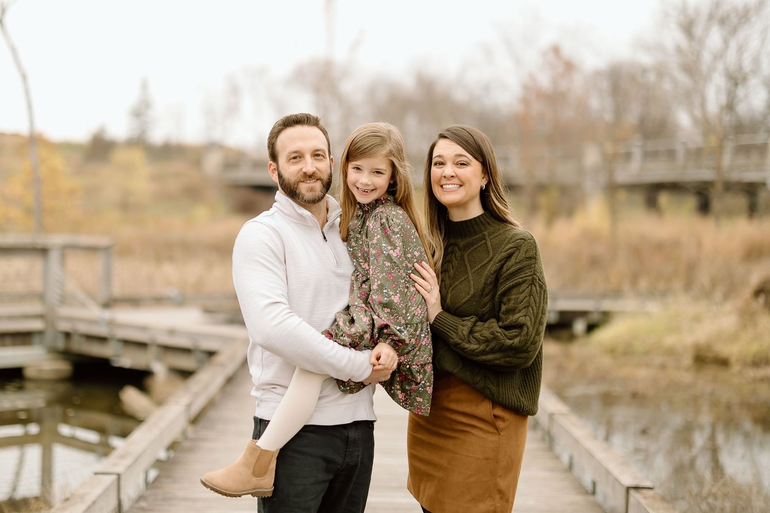 A family poses together on a wooden boardwalk over marsh water during an autumn photo session.