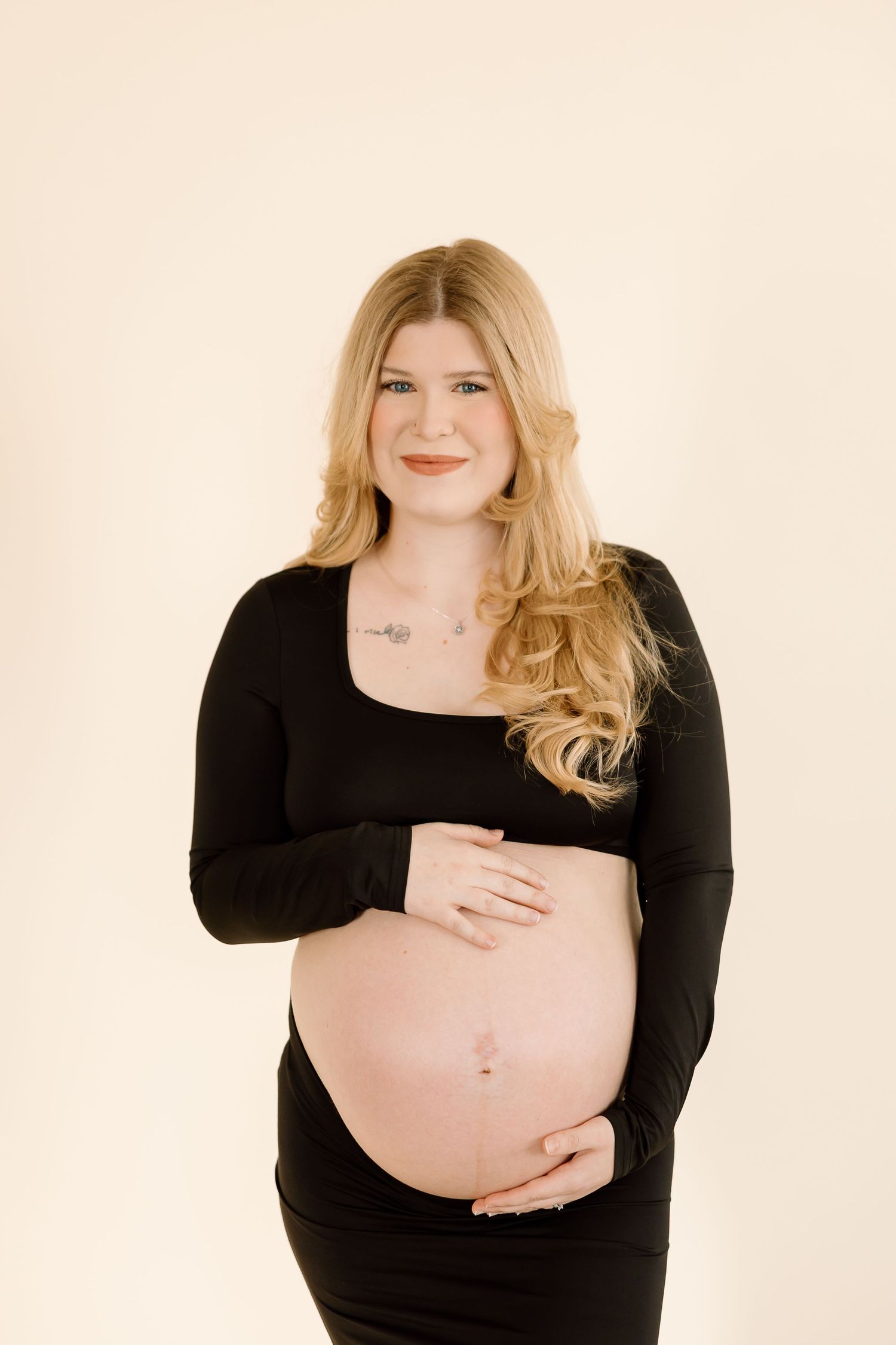 Pregnant woman in black long sleeve top smiles while cradling her baby bump.