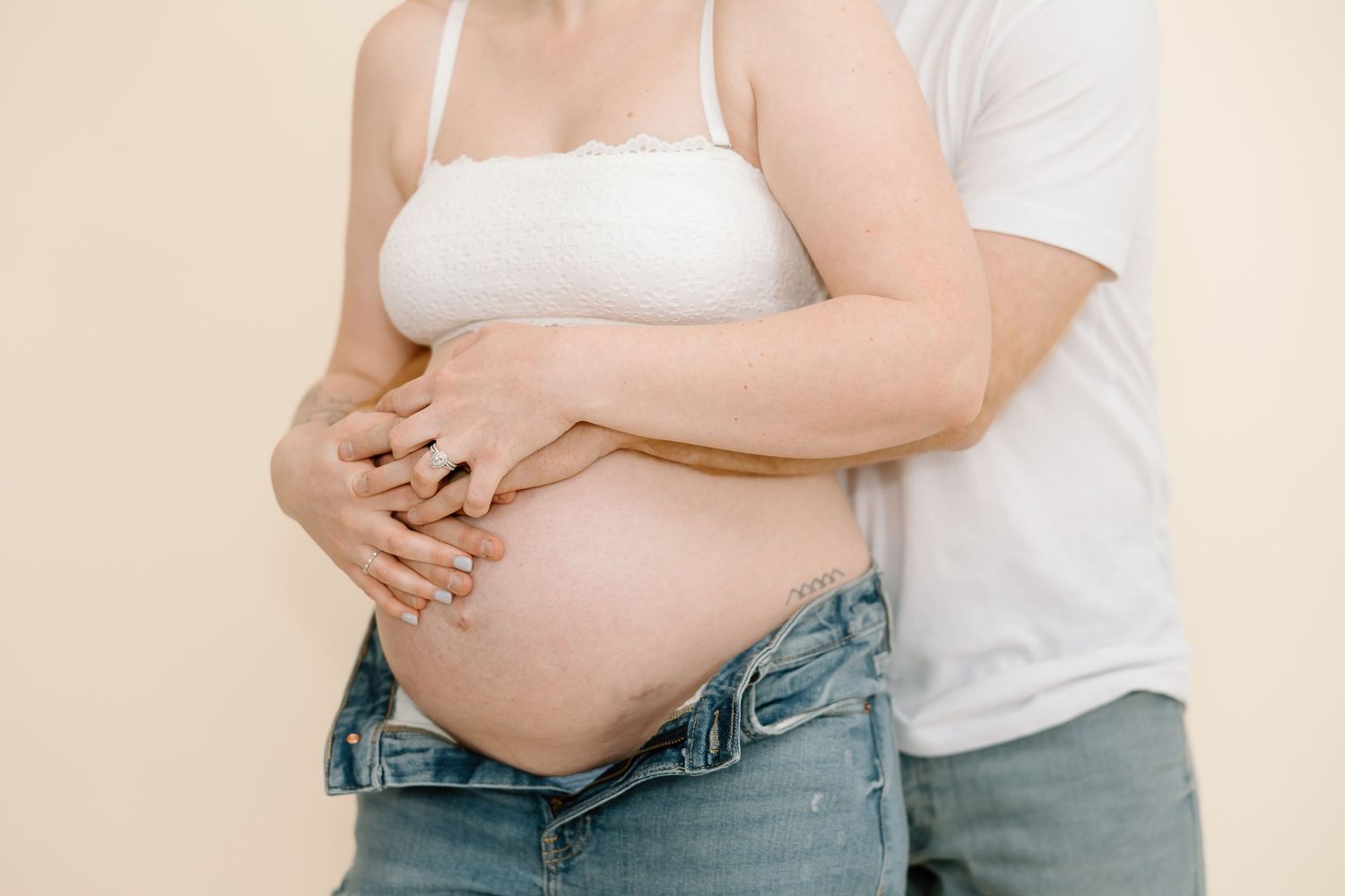 Close-up shot of hands cradling pregnant belly against neutral backdrop.