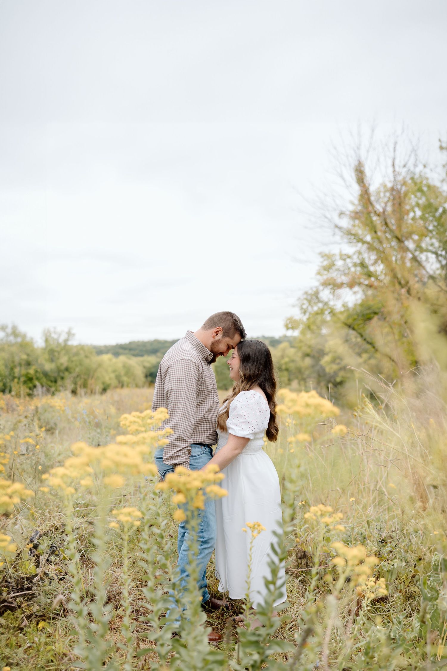 Intimate portrait of a couple sharing a close moment among tall grass and yellow flowers.