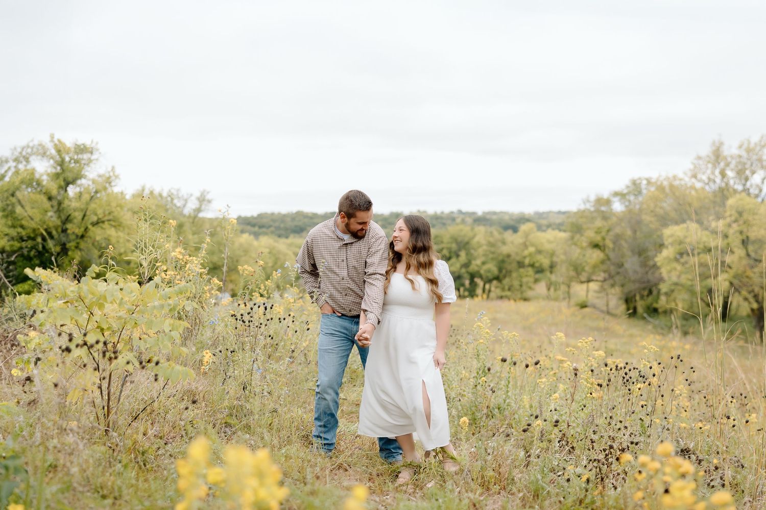 Couple laughing together while walking through a golden meadow on an overcast day.