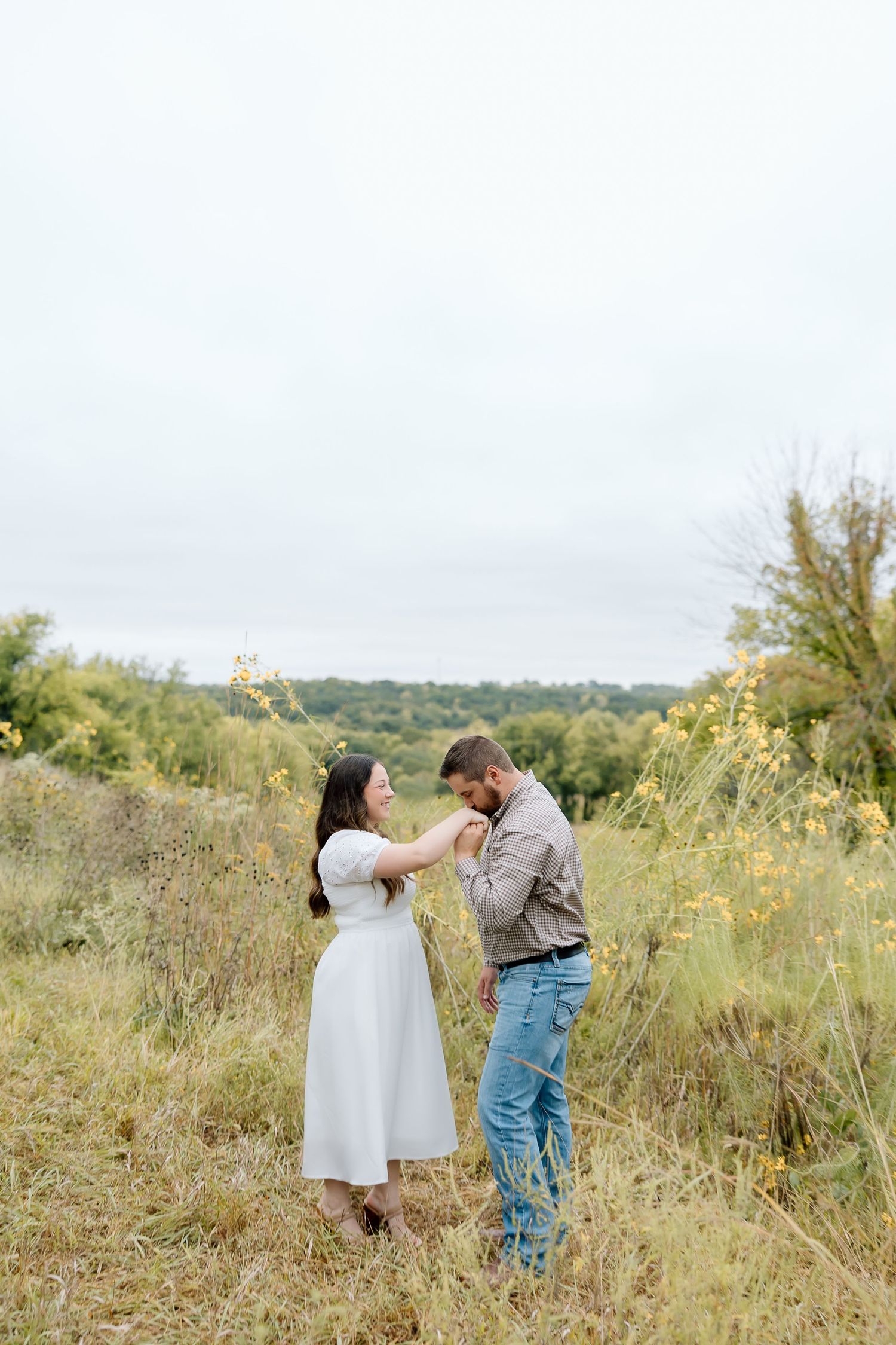 A couple dancing playfully in a wildflower meadow on a cloudy day.