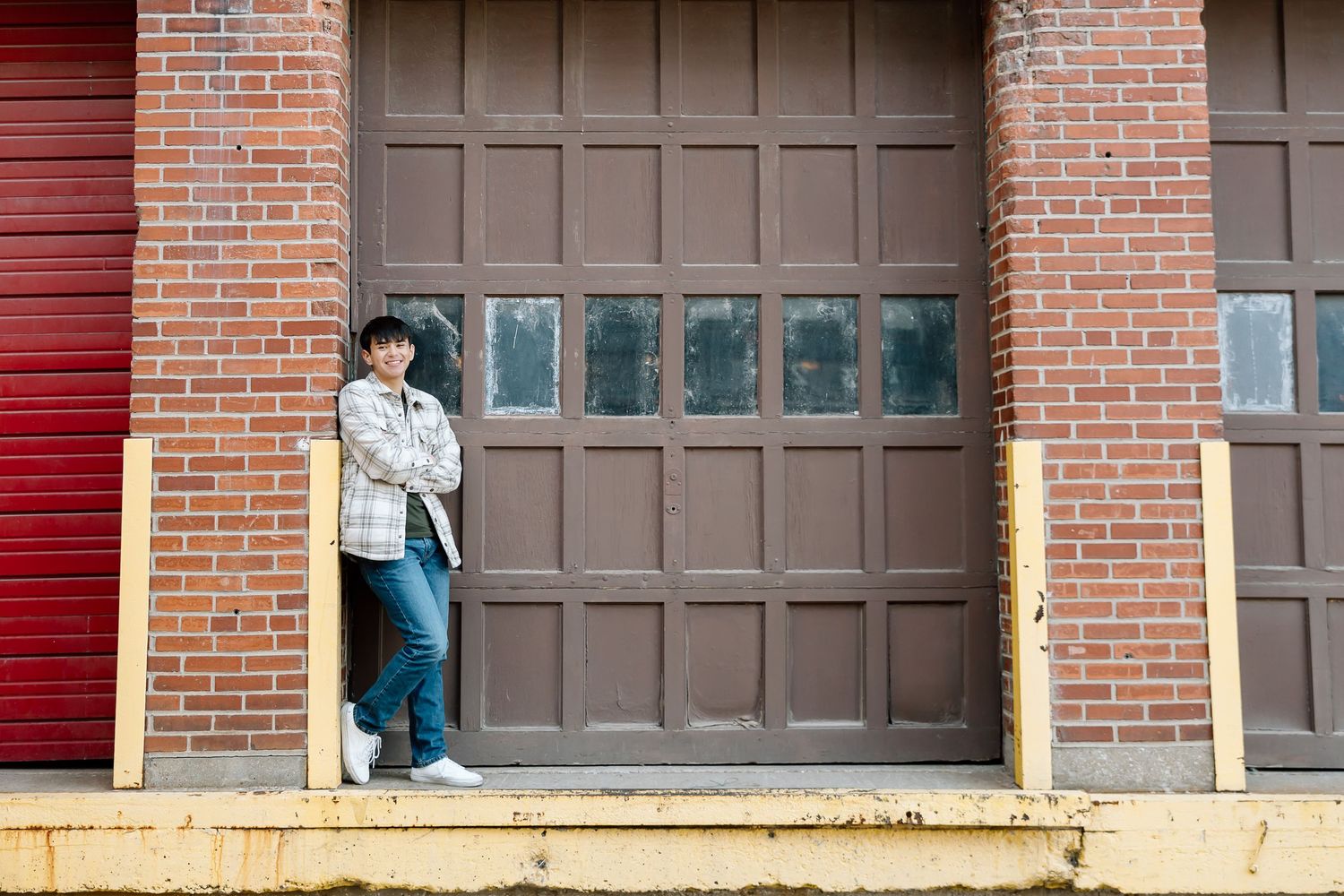 Person in plaid jacket and jeans standing on loading dock against brown industrial door.