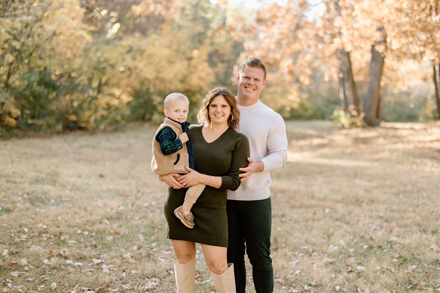 Family portrait outdoors with autumn foliage in background.