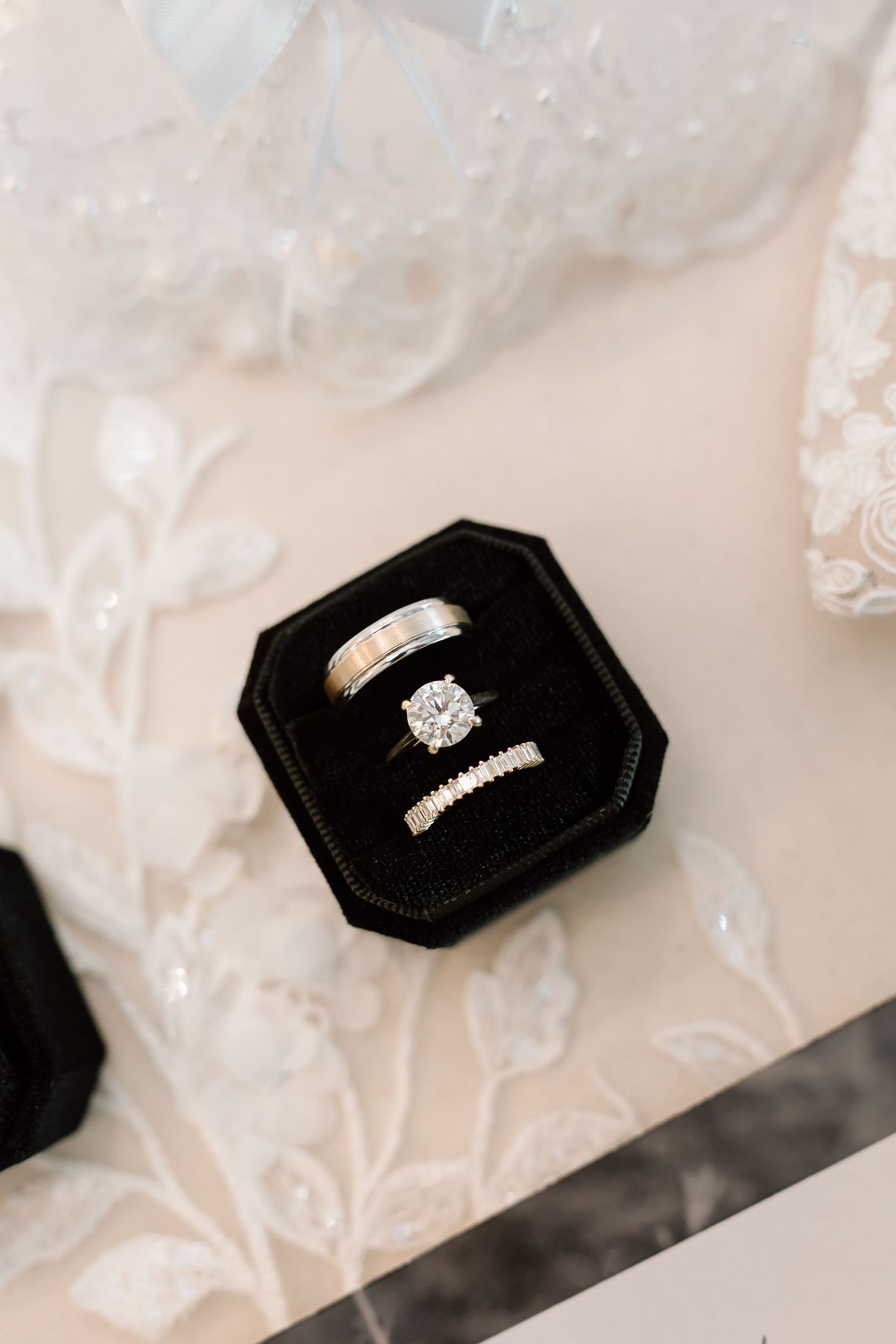 Wedding rings displayed in a black velvet hexagonal ring box with delicate lace fabric in the background.