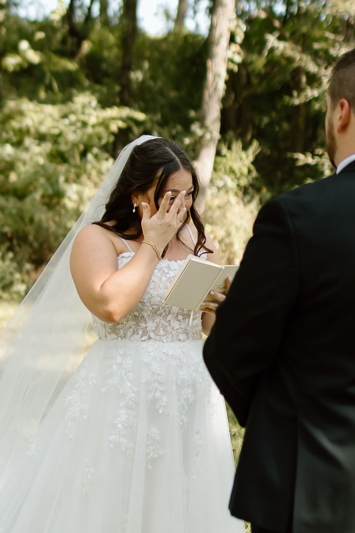 A couple shares an emotional moment while reading letters during their first look in a sunlit wooded setting.