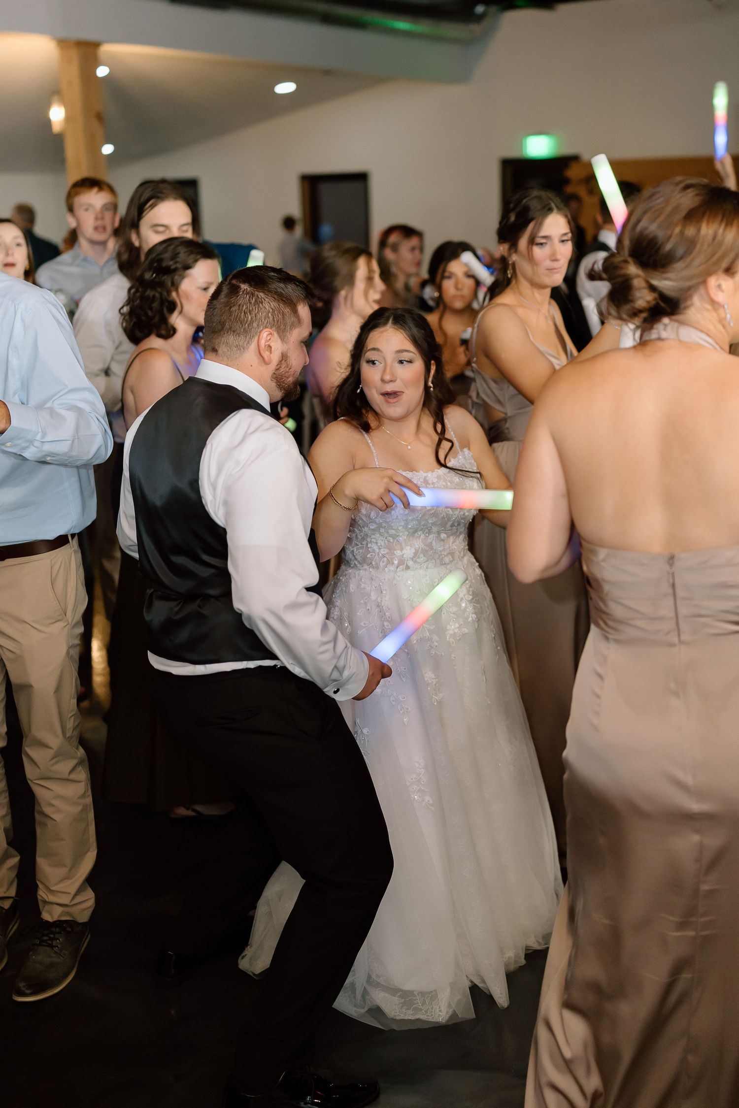 Wedding guests dance together at a reception with bridesmaids in beige dresses and groomsmen in light colored suits.