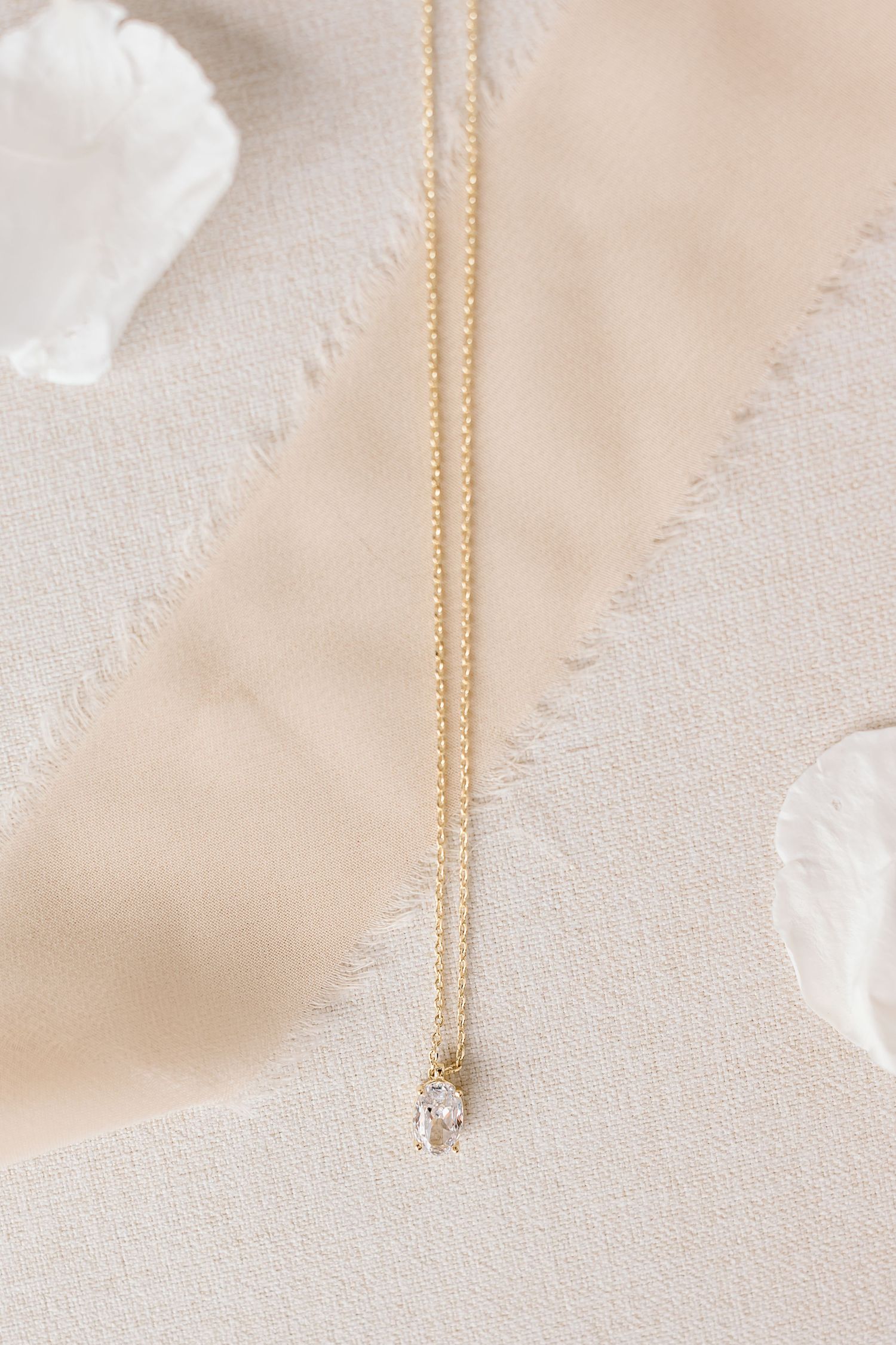 Delicate gold chain necklace with small crystal pendant displayed on beige textured fabric background.