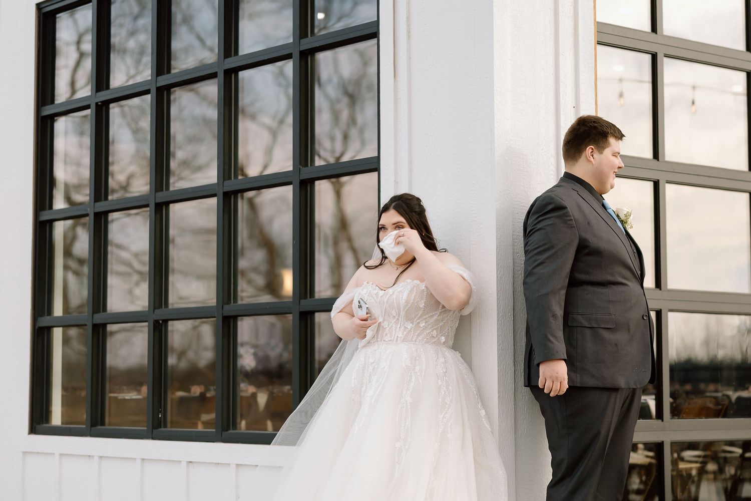 A bride and groom share an intimate moment together in front of large industrial windows at their wedding venue.