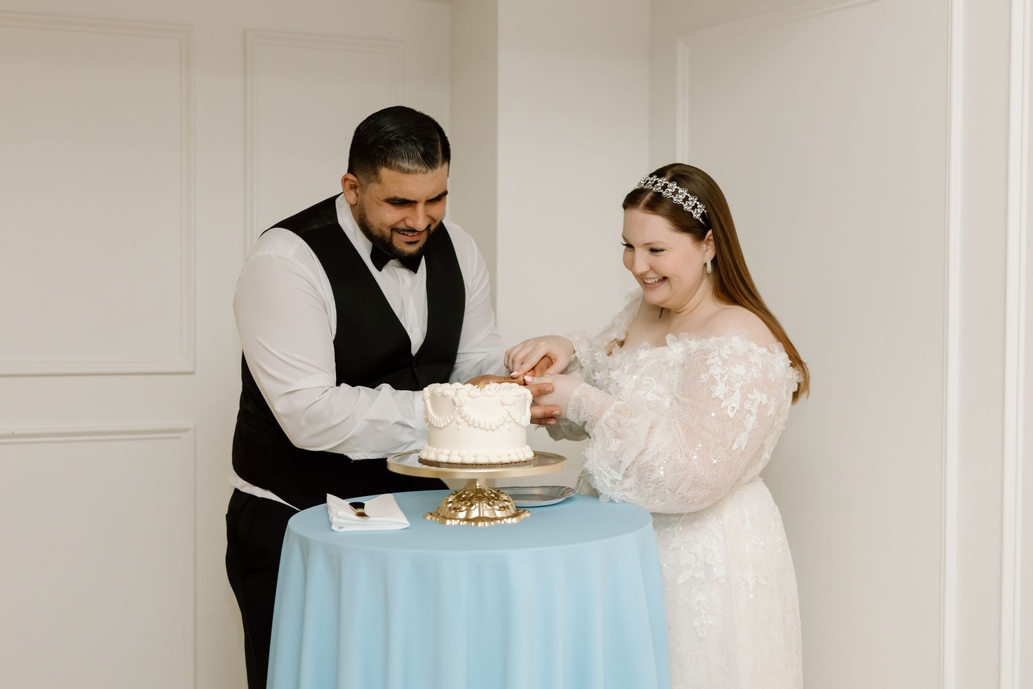 Bride and groom cutting their white wedding cake on a blue table during their wedding reception.