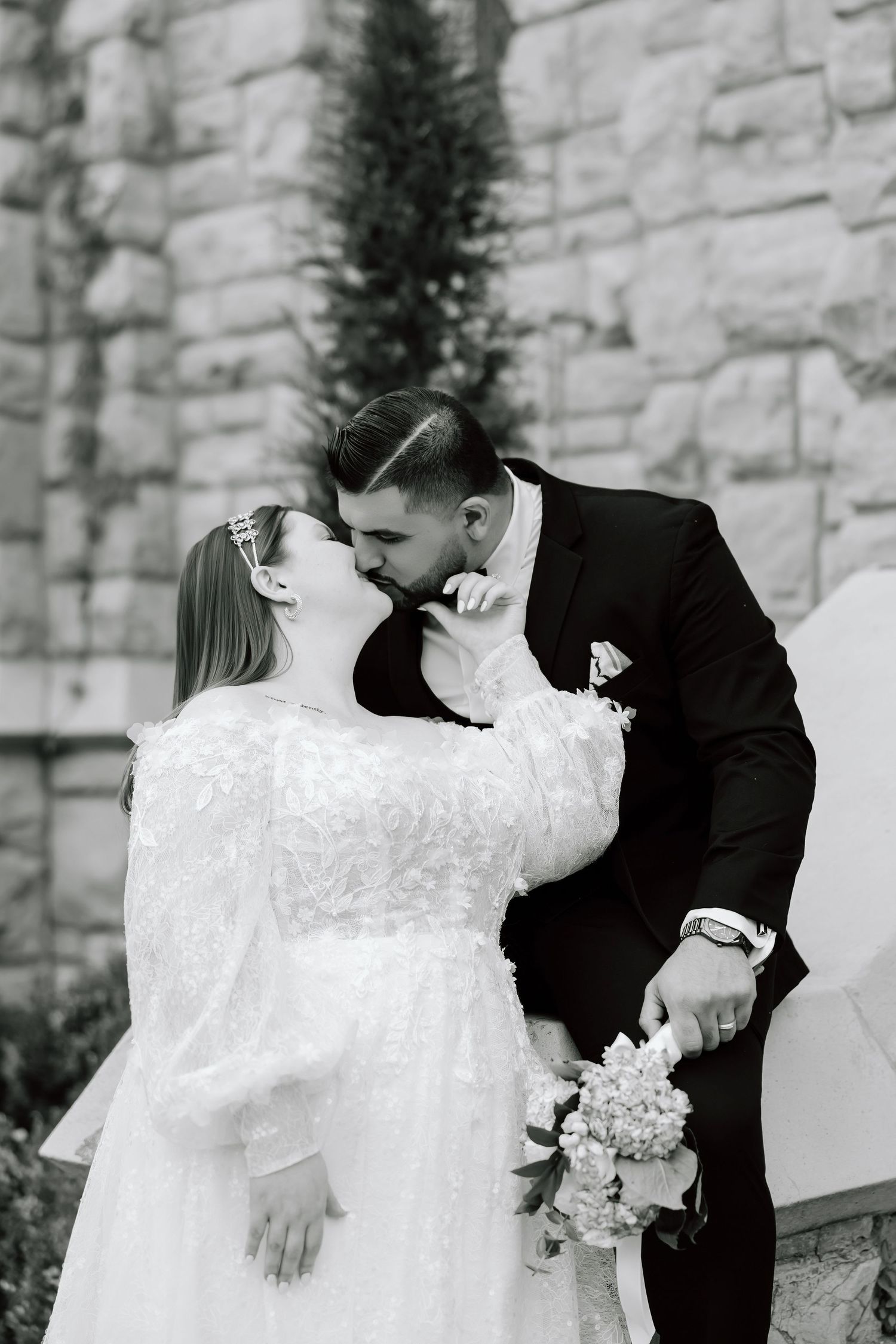 Black and white photo of a bride and groom sharing a kiss at their wedding ceremony outdoors.