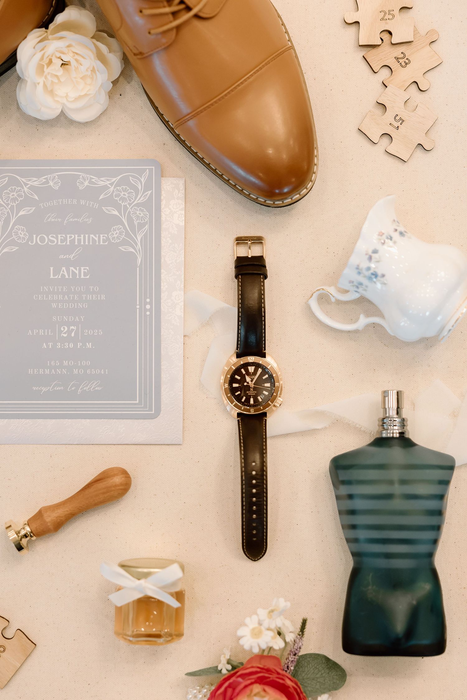 Flatlay arrangement of luxury accessories including brown leather shoes, watches, perfume bottles and delicate paper items.