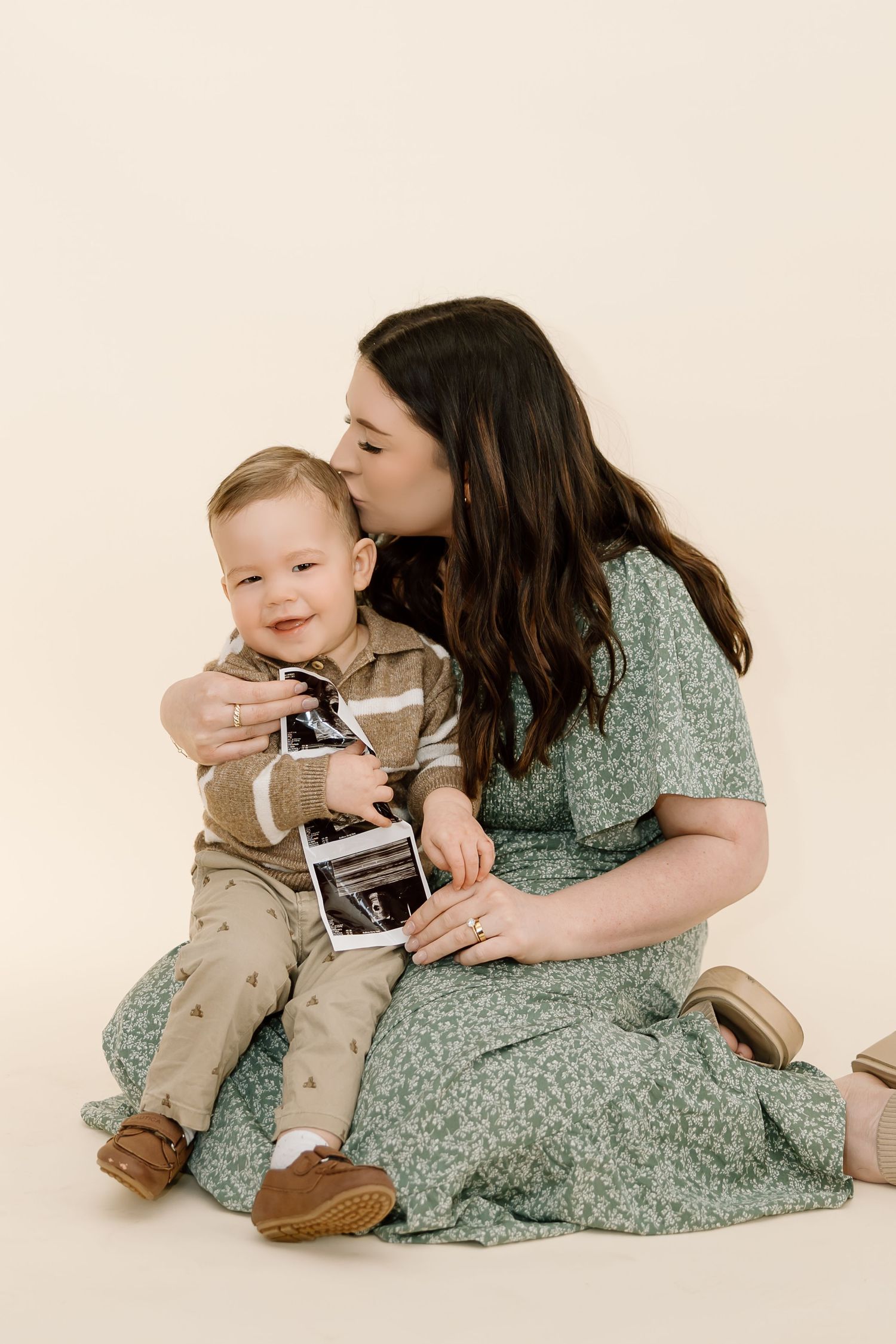 A tender moment between parent and baby in matching green and khaki outfits during a studio photoshoot.