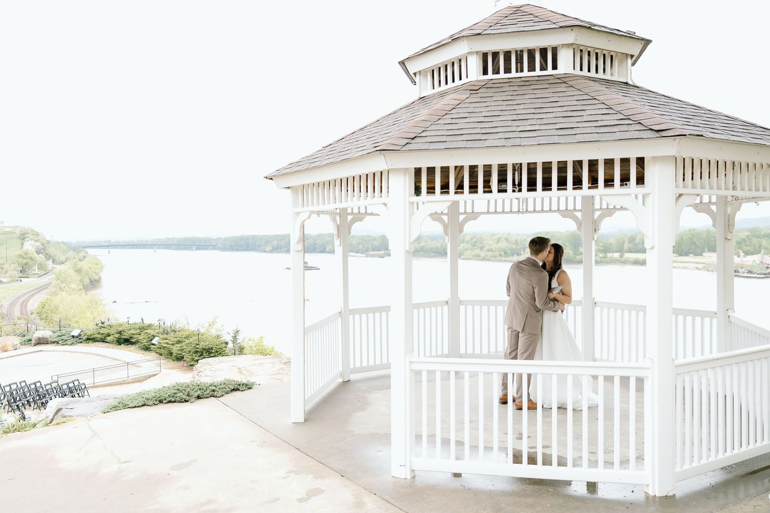 A white wooden gazebo with ornate details stands on a landscaped lawn overlooking a scenic view.