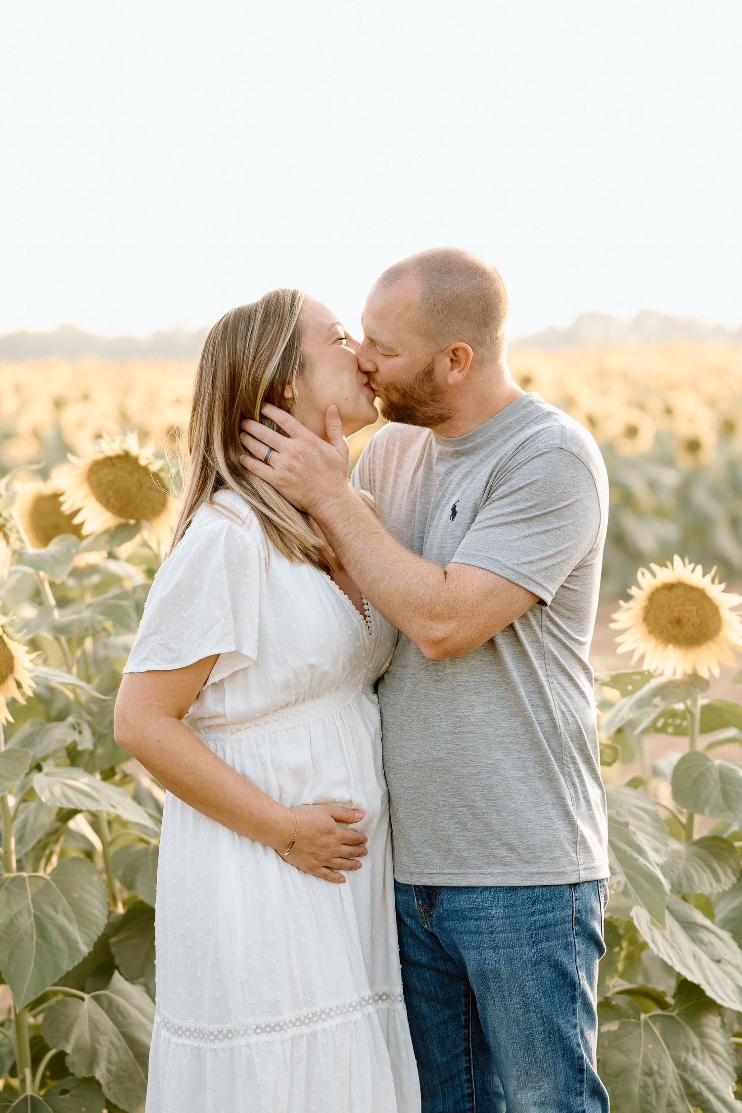 A couple shares an intimate moment in a sunlit sunflower field during a romantic photoshoot.