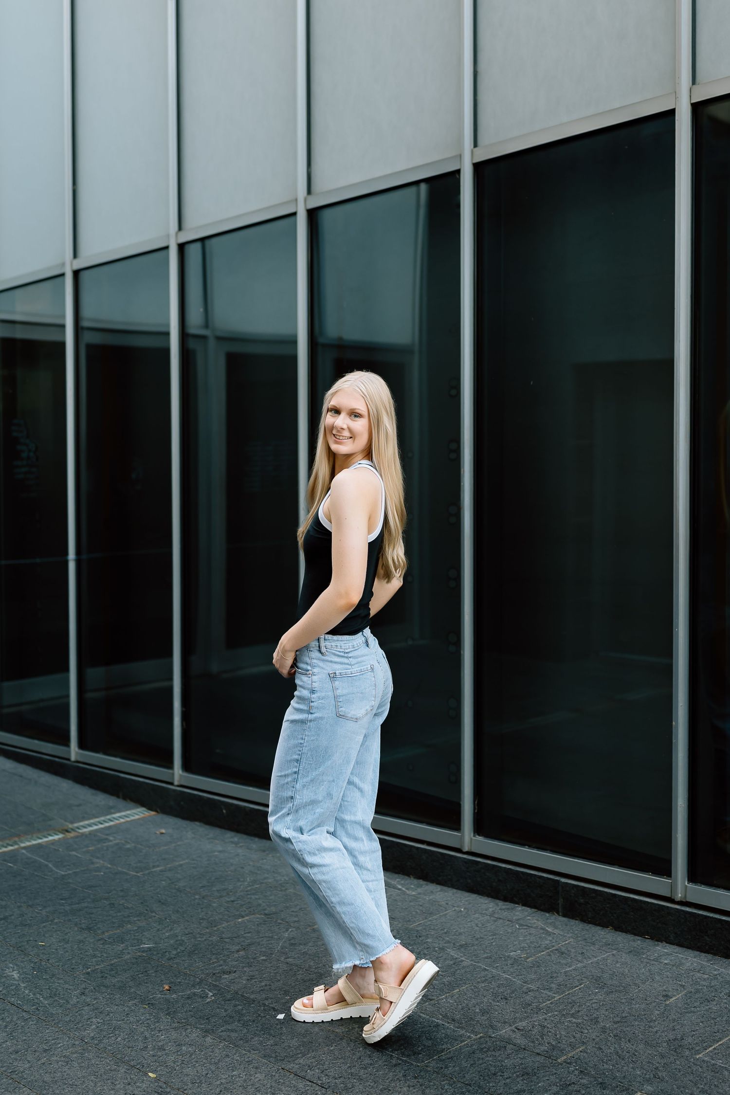 A person wearing denim overalls poses playfully against a modern glass building exterior.