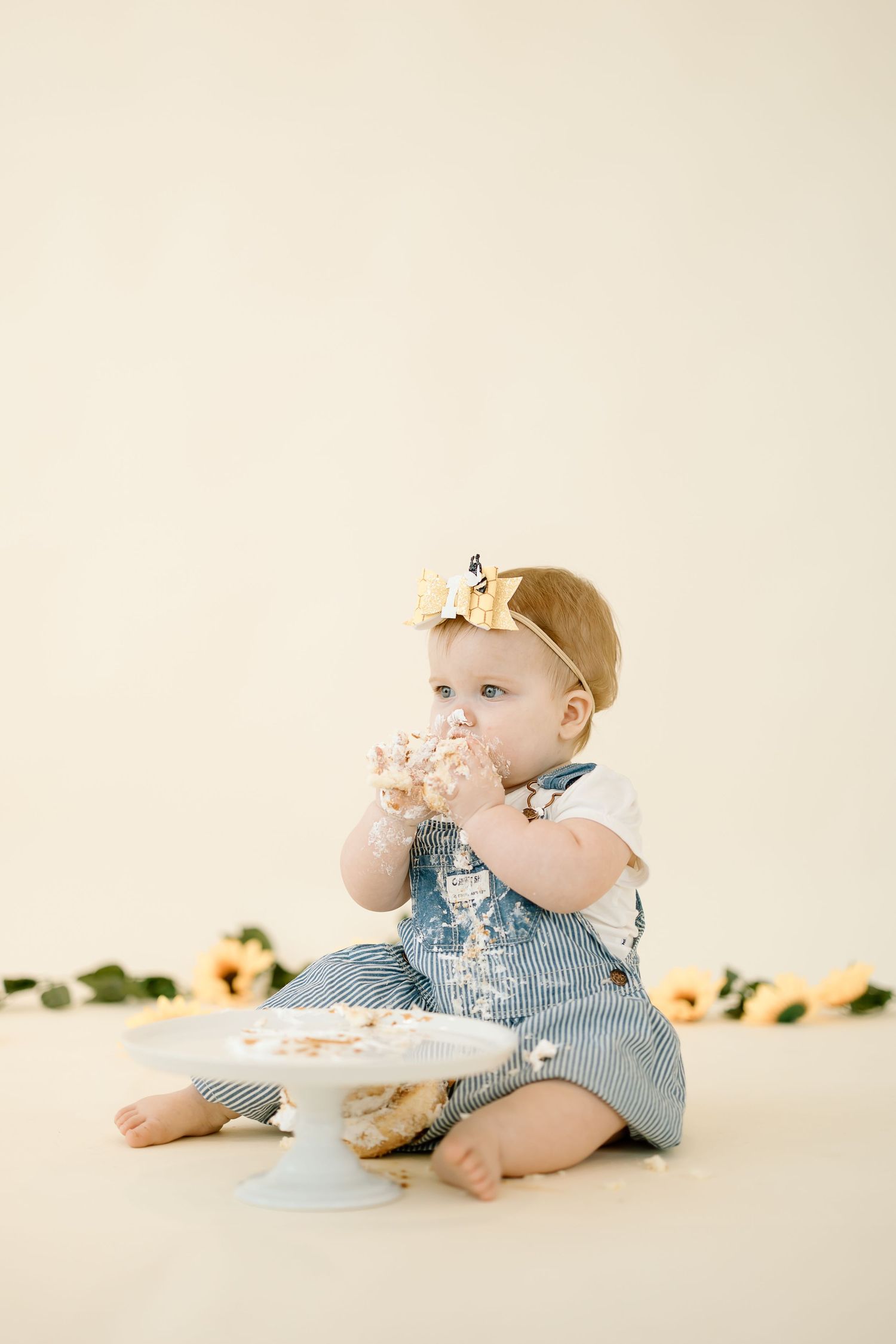 A baby in blue overalls enjoys a cake smash photo session with three progressive stages of messy cake eating.