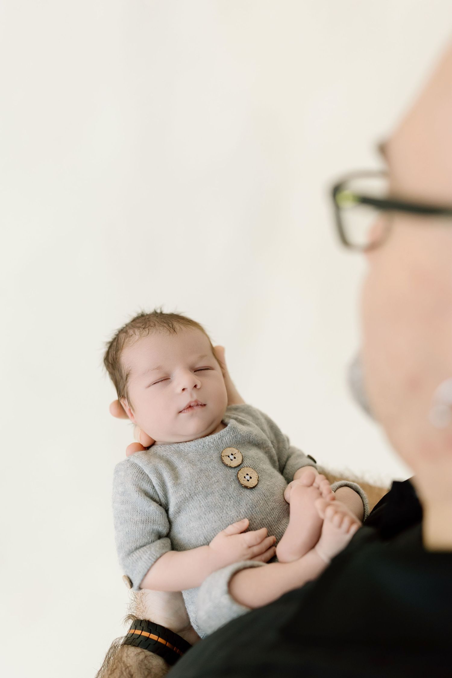 A sleeping baby wearing a gray sweater with buttons rests peacefully on someone's shoulder.