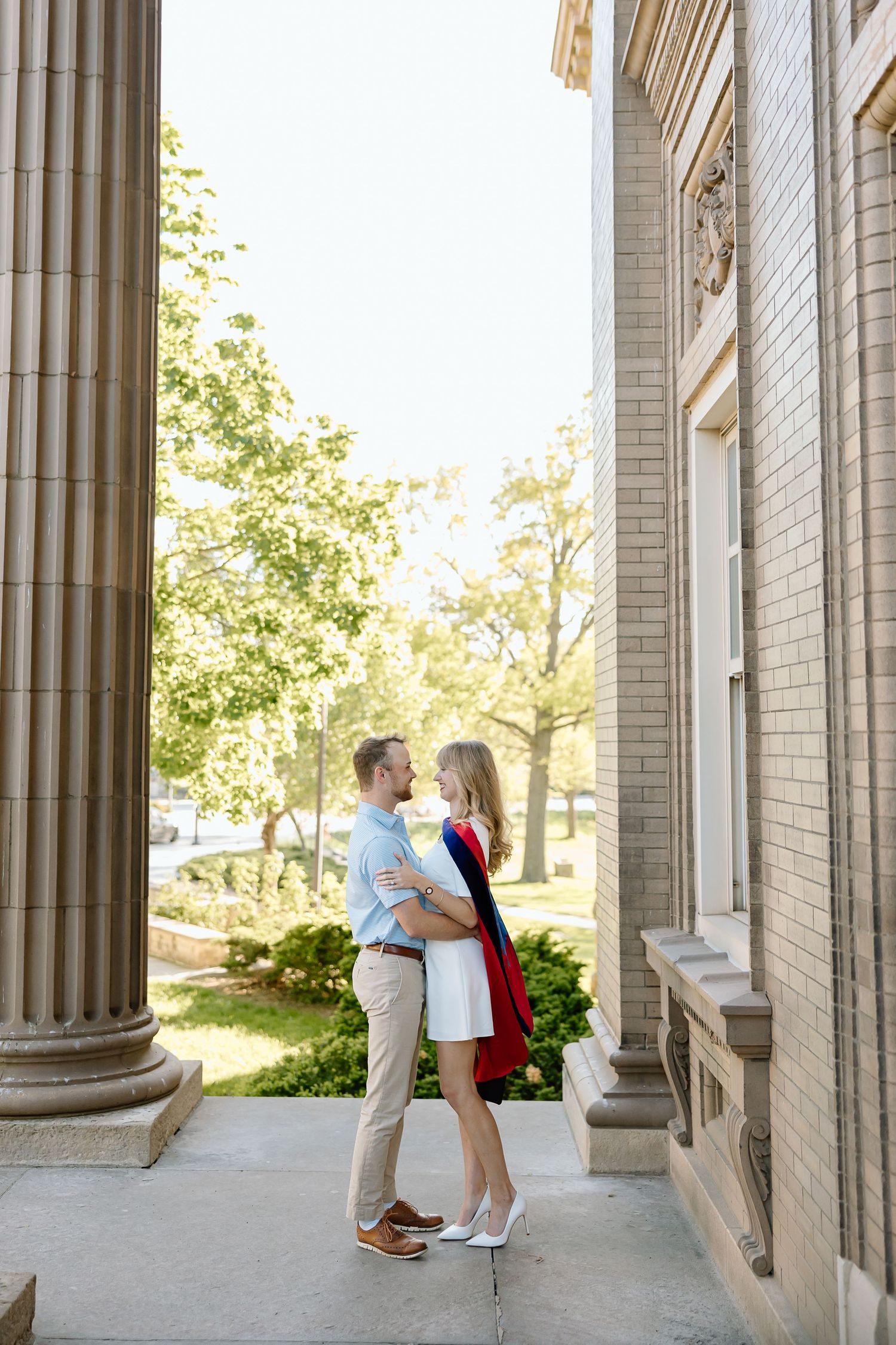 Romantic couple shares intimate moments between elegant white columns in a classic architectural setting.