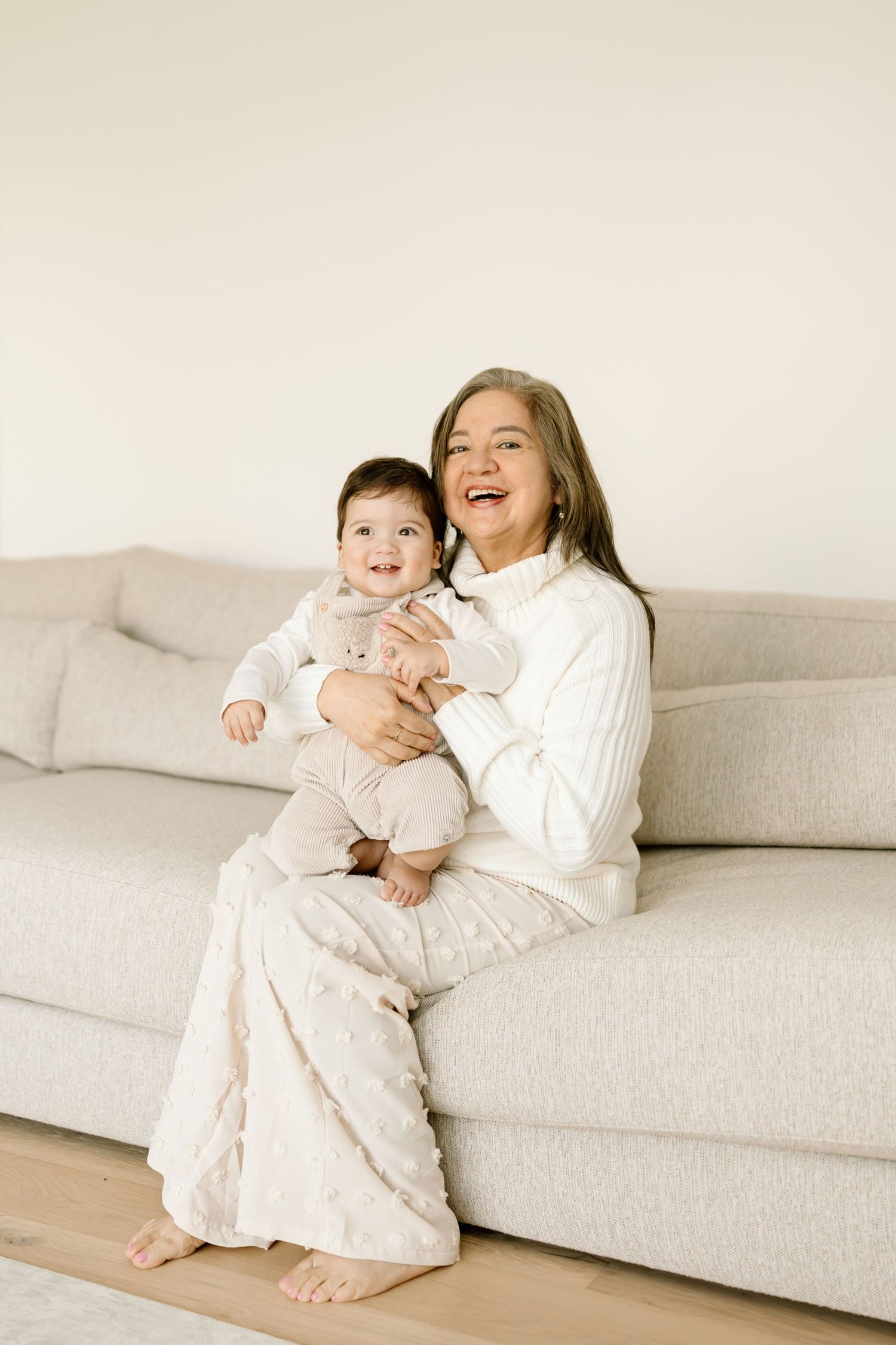 Two people in white outfits share tender moments while relaxing together on a light gray couch.