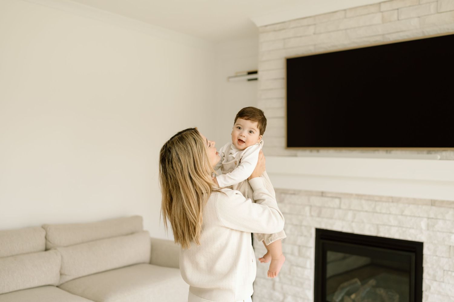 A parent and baby share playful moments together on a white couch in a bright modern living room.