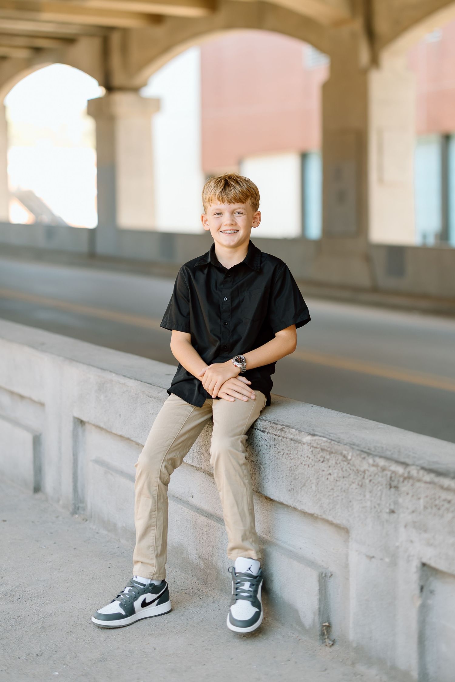 Children sit on a concrete ledge in a covered outdoor space wearing casual clothing.