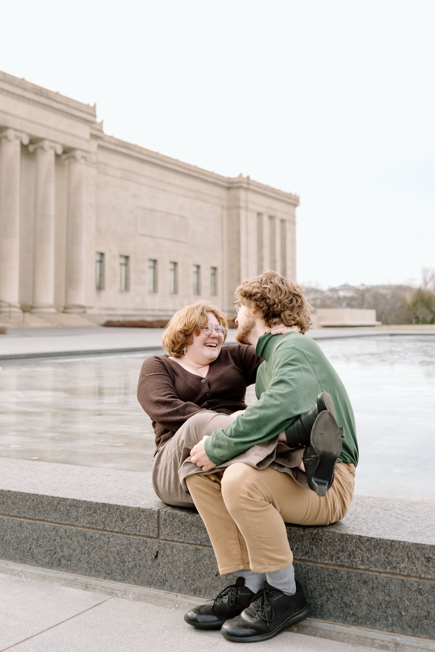 A couple sits together and shares a joyful moment on stone steps outside a neoclassical building with columns.