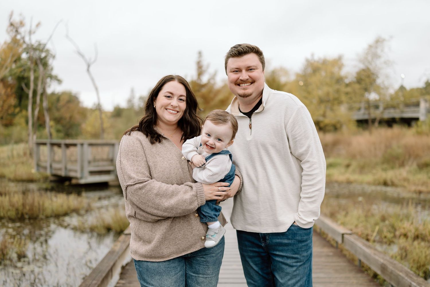 A family enjoys a tender moment together on a wooden bridge during an autumn outdoor photo session.