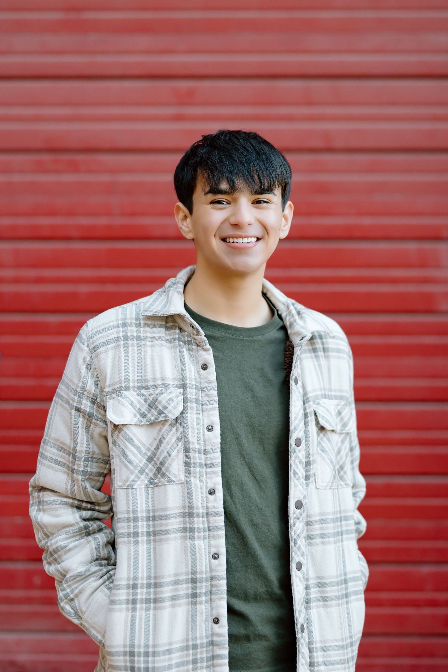 Person wearing plaid jacket and green shirt smiling against vibrant red background.