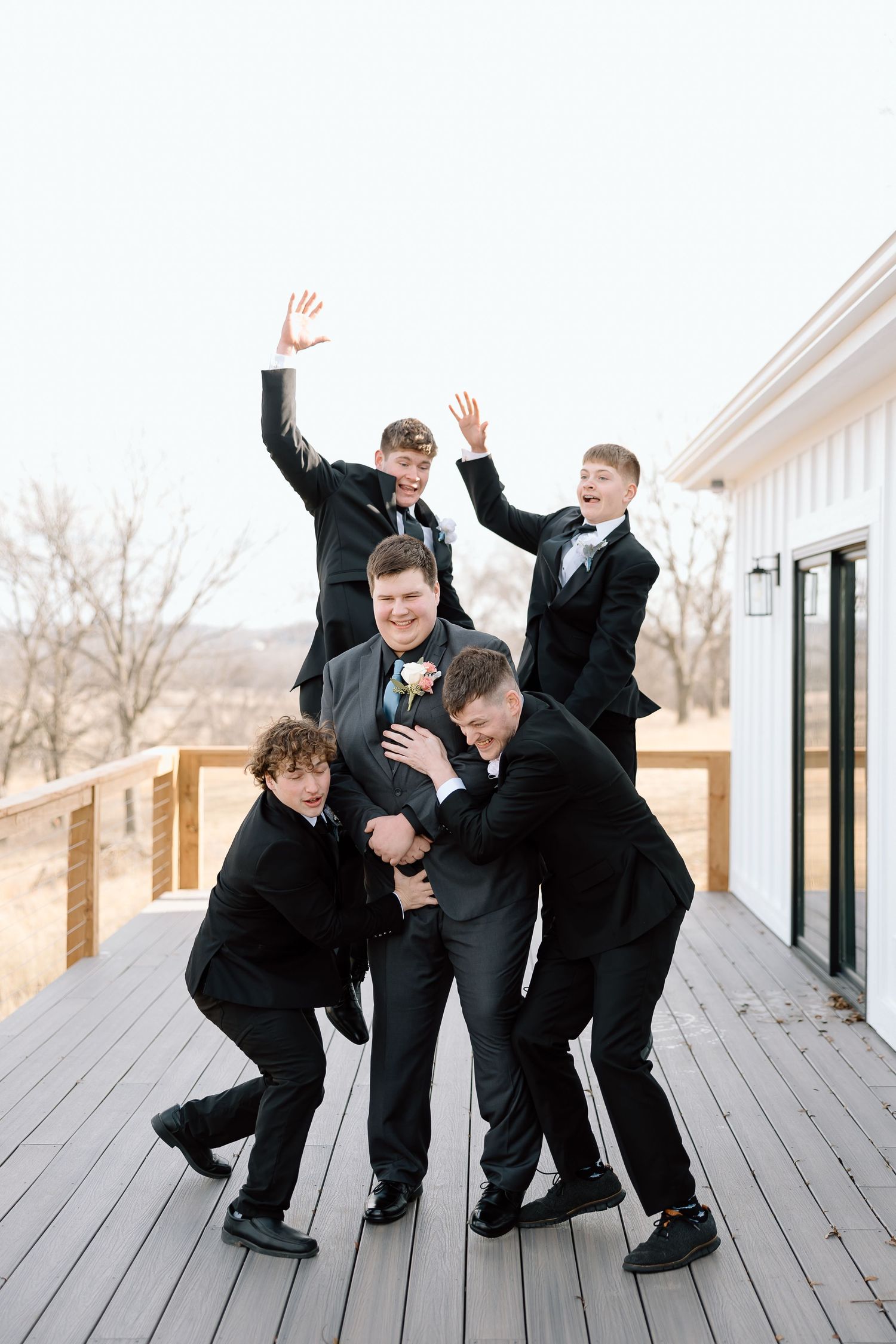 Groomsmen playfully tackle groom in fun group photo on deck.