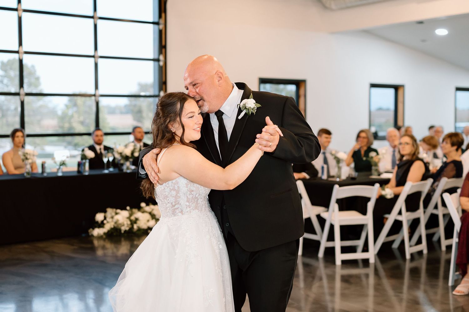 A couple shares an intimate dance moment at an indoor wedding reception with guests seated in the background.