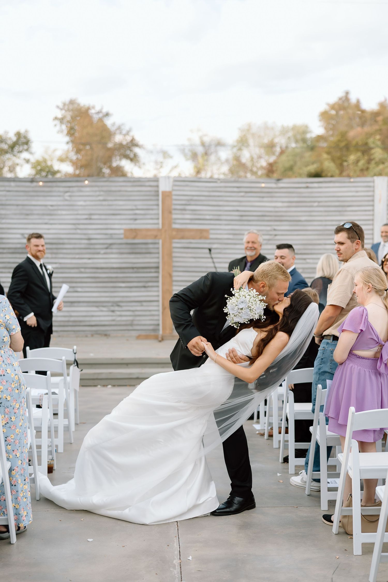A sequence of wedding ceremony photos showing a couple dipping and kissing at an outdoor venue with white chairs.