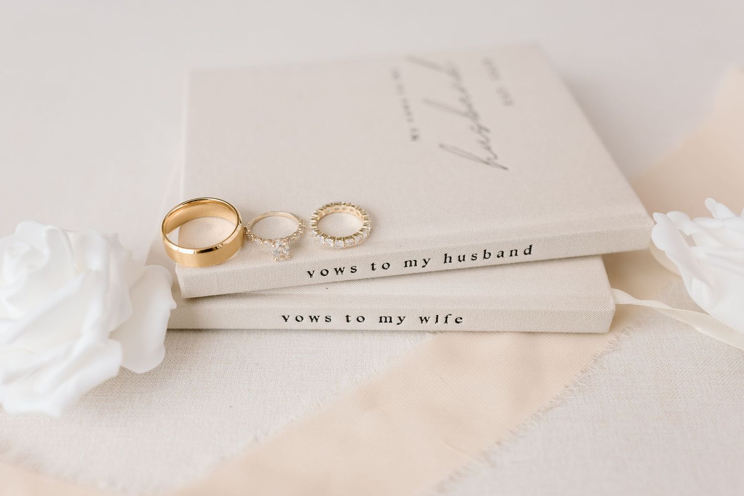 Wedding vows books for husband and wife with gold and silver wedding rings displayed on white fabric.