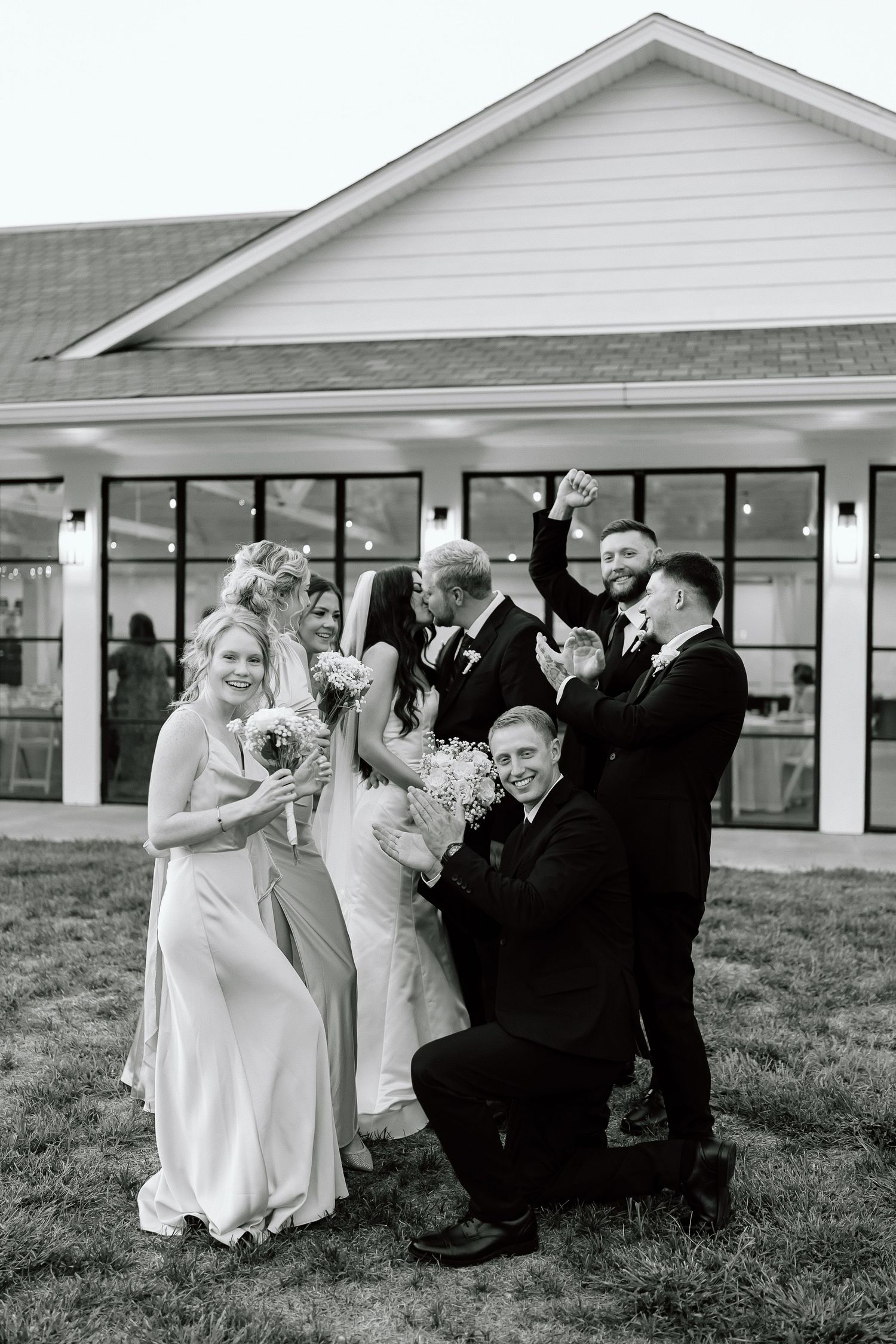 Black and white photo sequence of wedding party posing and laughing together on grass in front of white building.