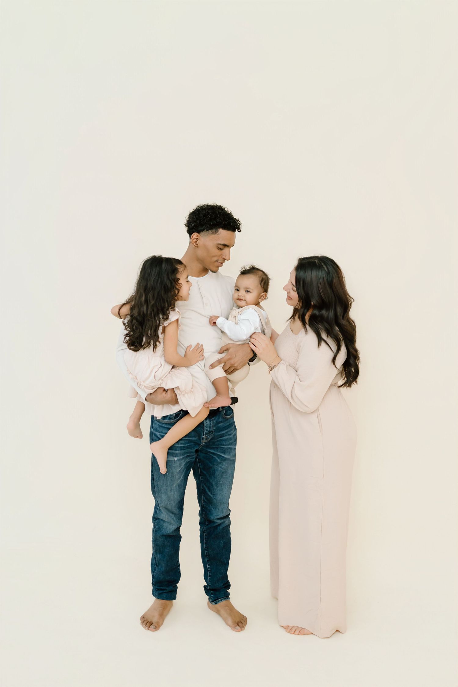A family in white and neutral colors poses together against a plain white backdrop for a minimalist portrait.