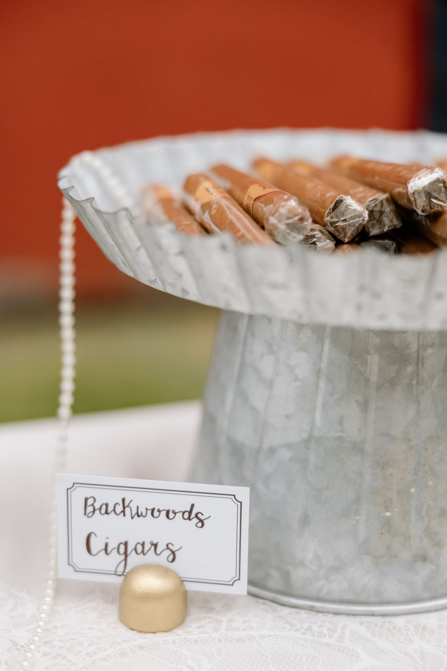 Galvanized metal bucket filled with Backwoods cigars displayed on a white lace table with a gold ball sign holder.