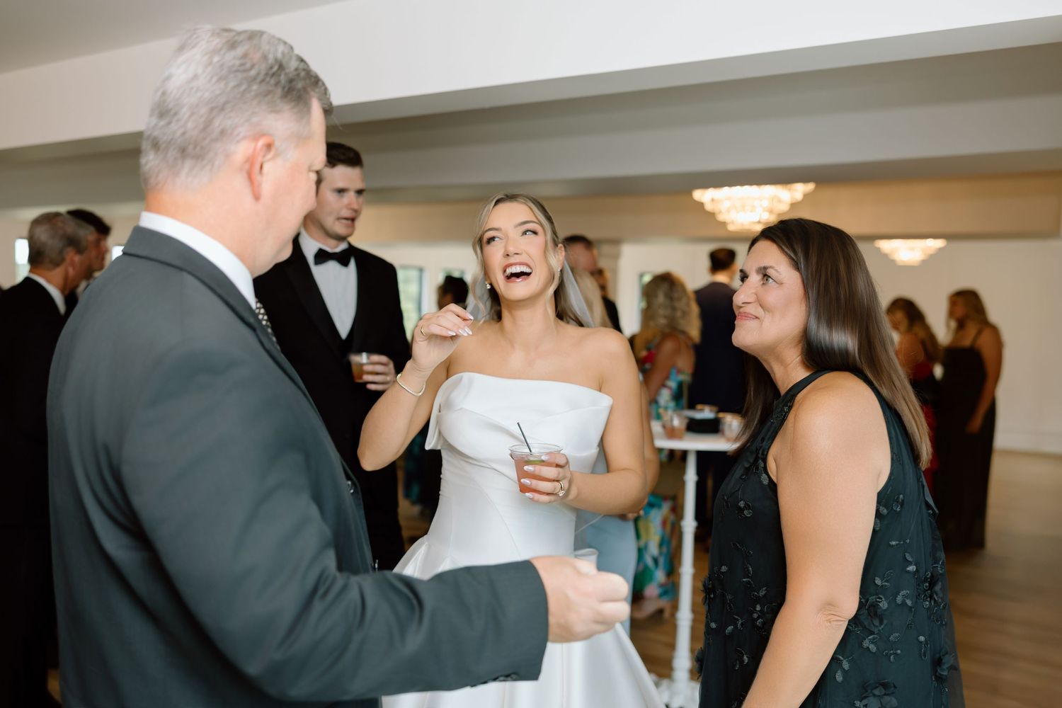 Bride in white strapless gown laughing with guests at elegant wedding reception venue.