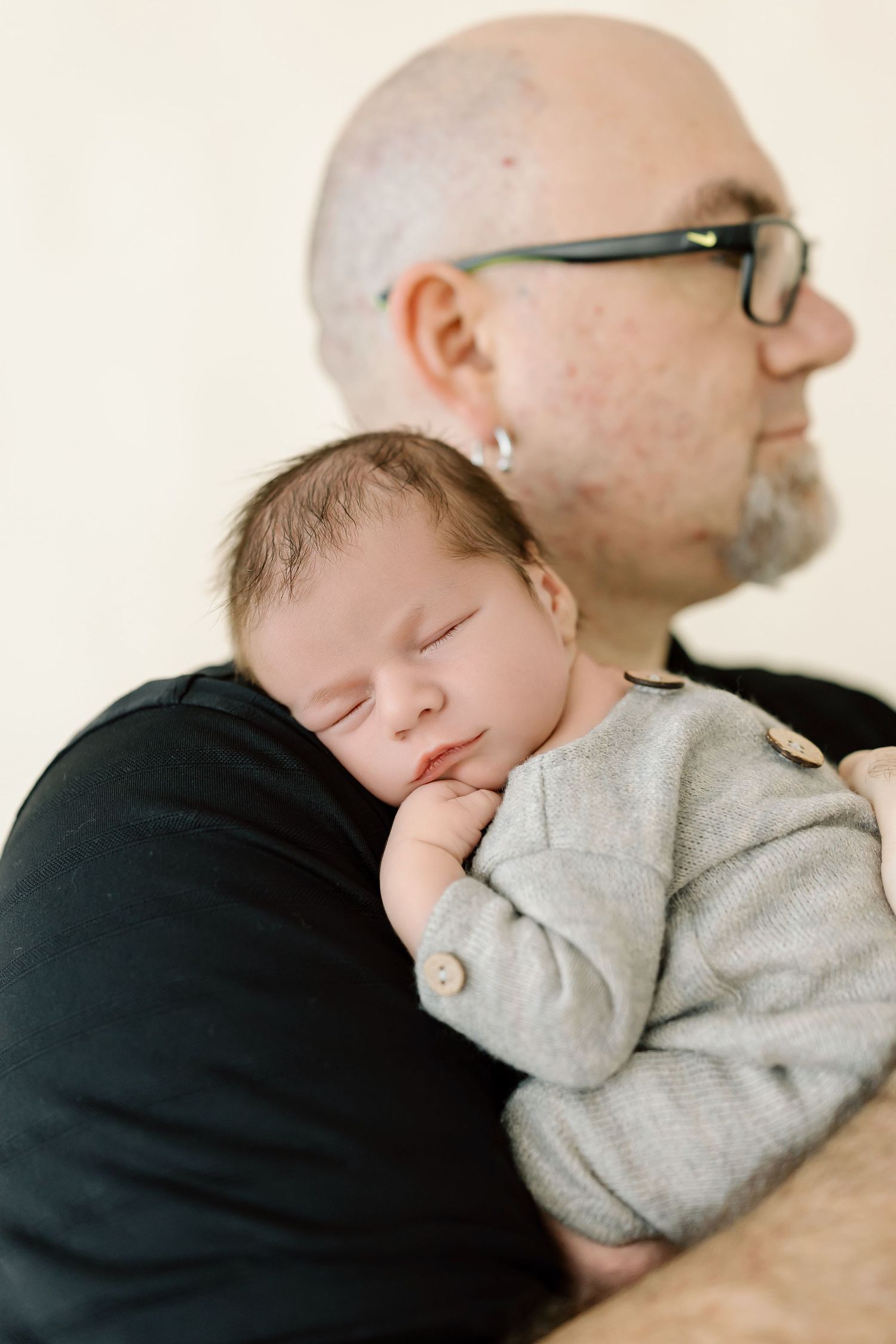 A sleeping baby rests peacefully on someone's shoulder wearing a cozy gray sweater.
