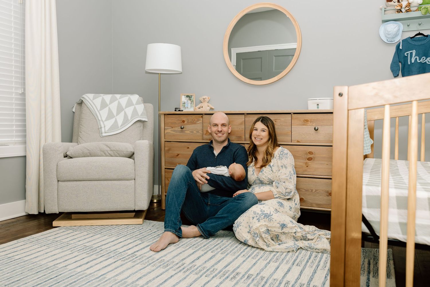 Stylish nursery interior with natural wood crib, round mirror, and modern gray and white decor elements.