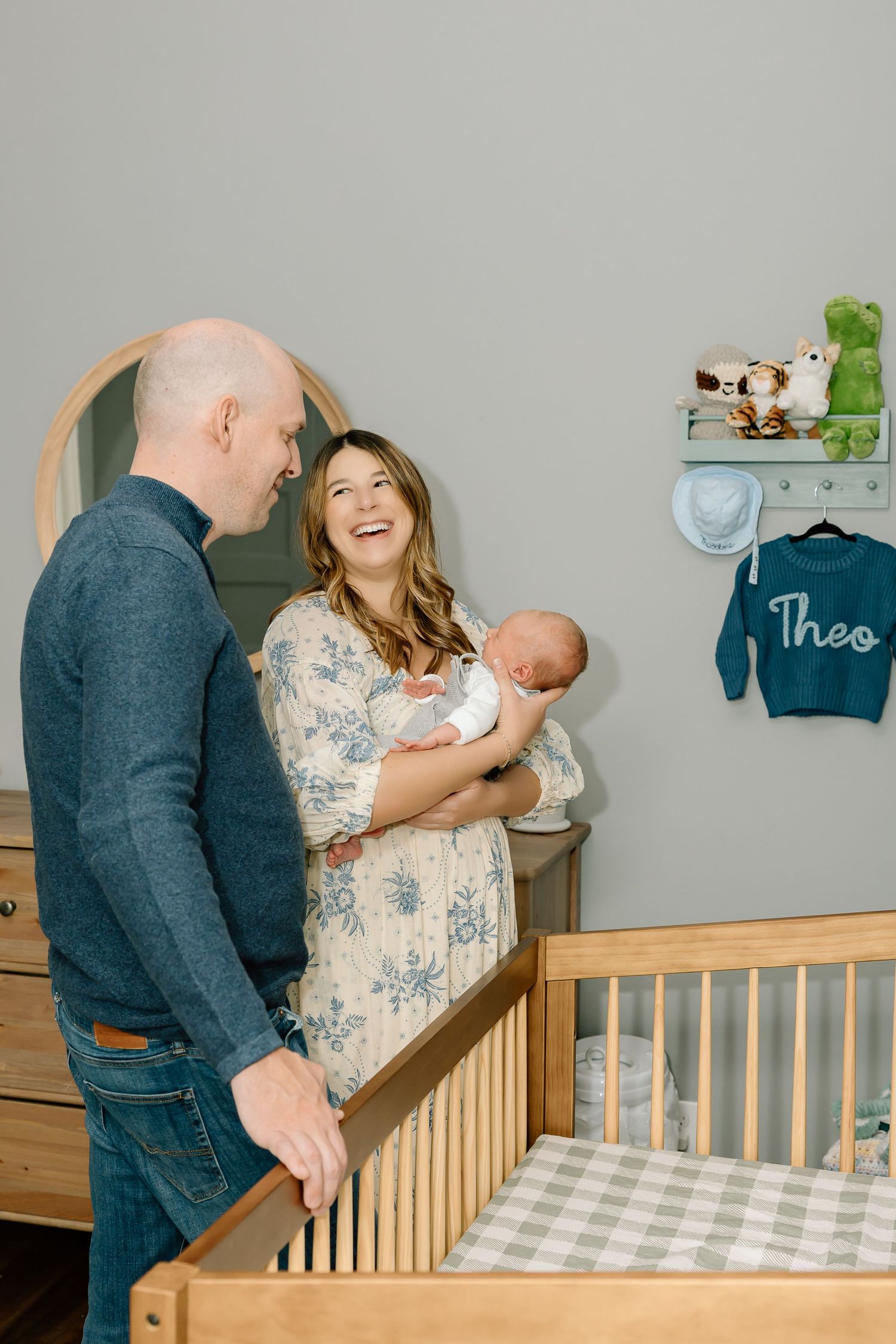 Parents share tender moments with their baby near a wooden crib in a nursery decorated with soft blue and green accents.