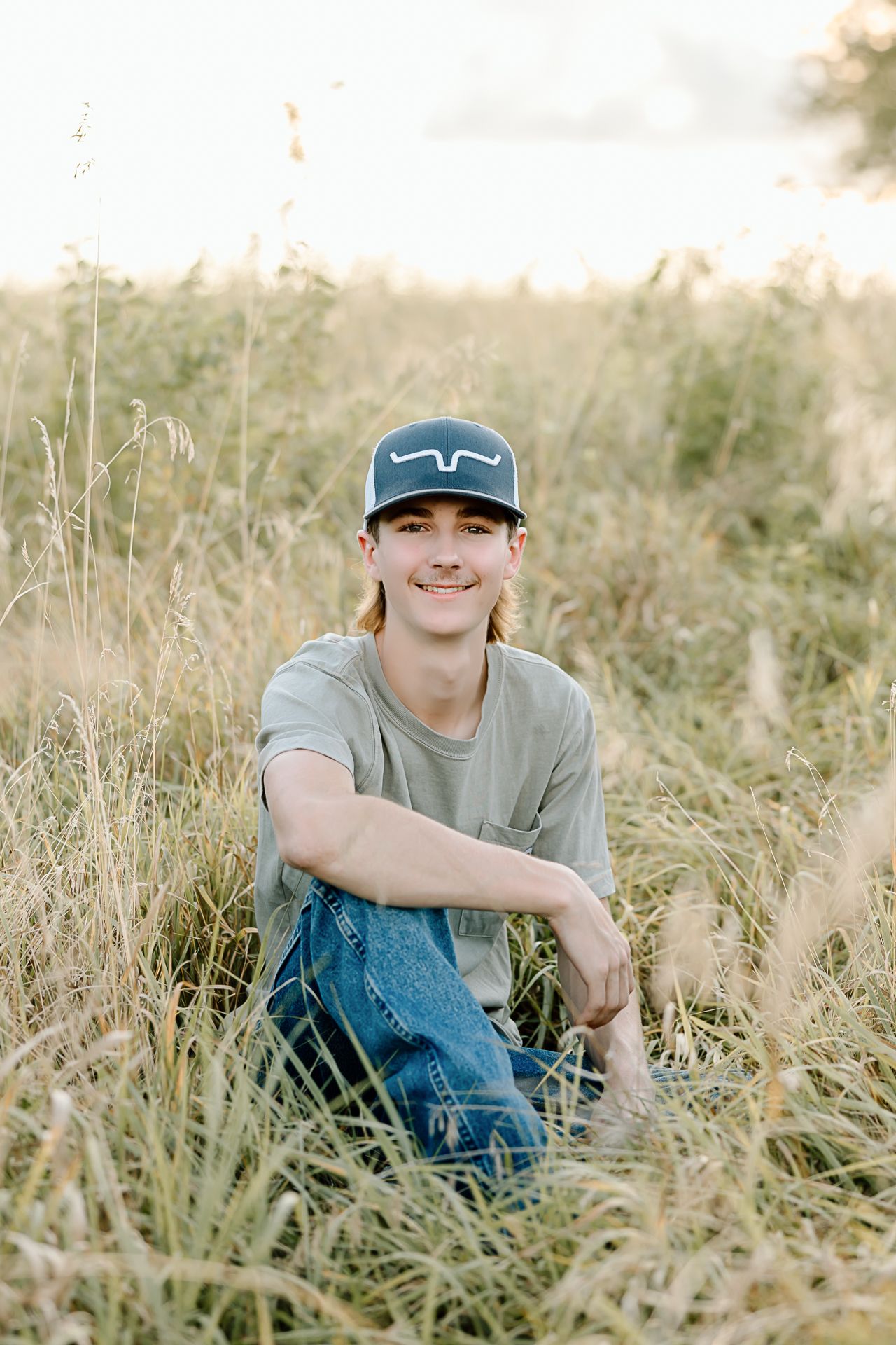 Four candid outdoor portraits of someone sitting in tall grass wearing jeans and a gray t-shirt on a sunny day.