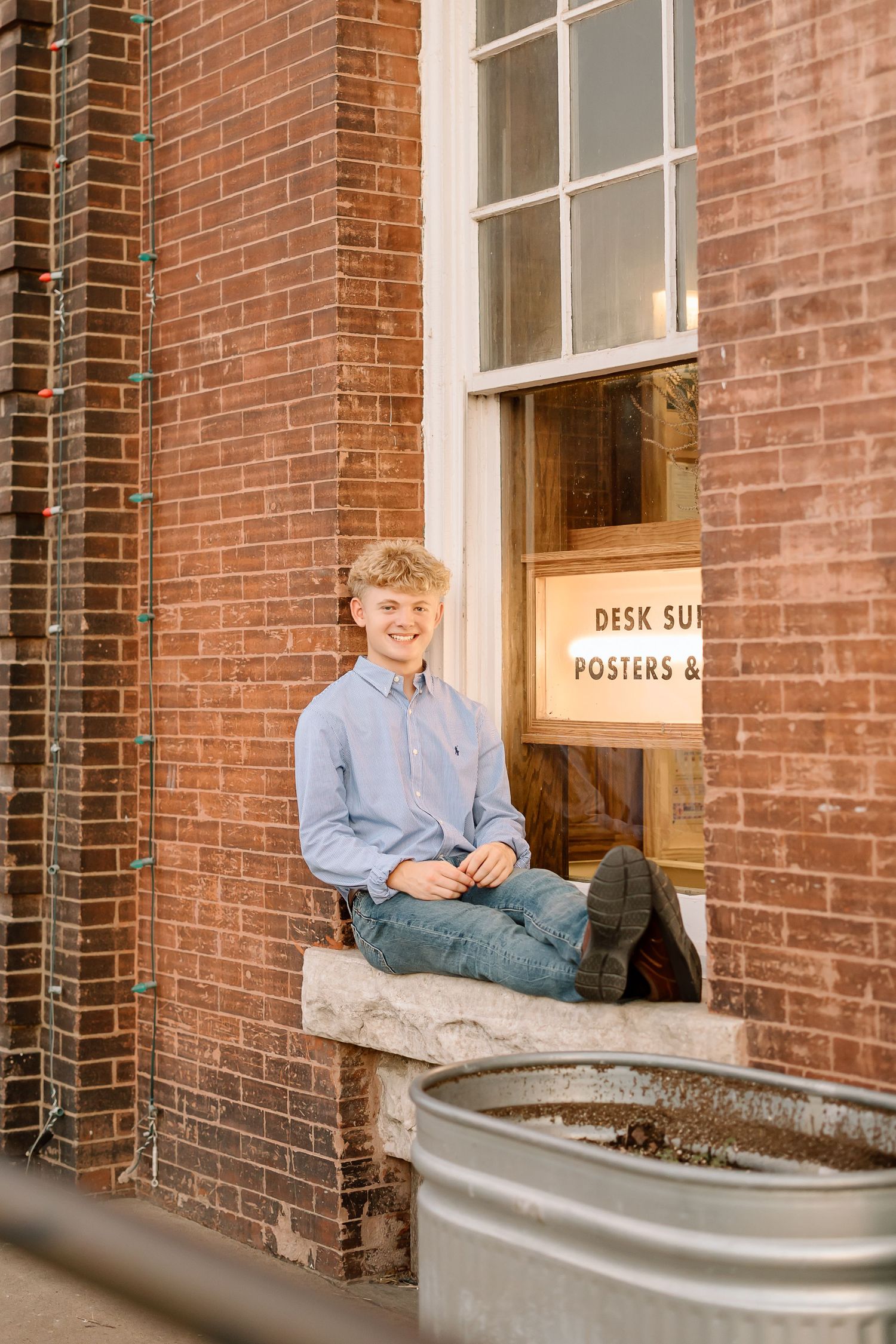 Someone sits casually in a window ledge of a historic red brick building on a sunny day.